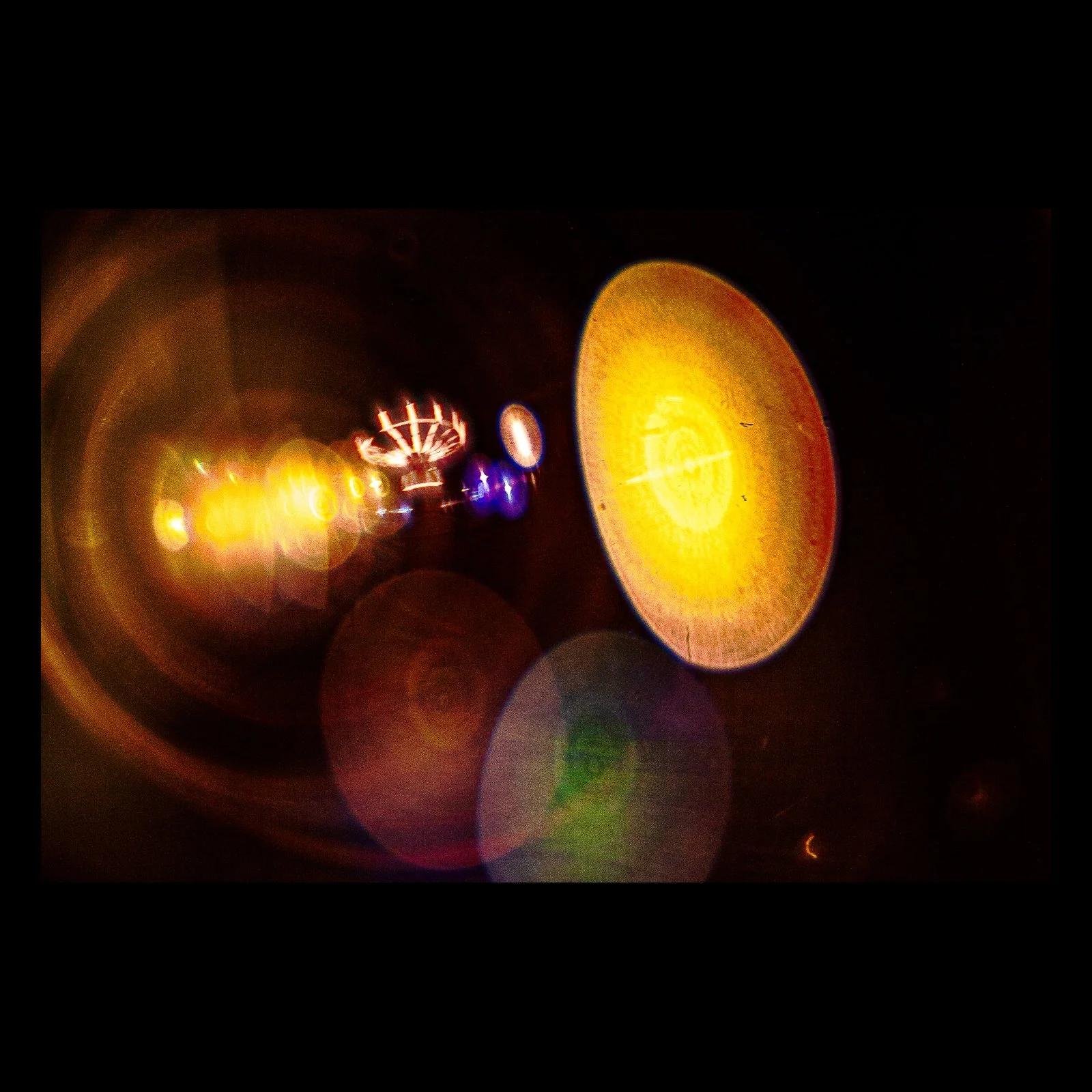 Full-frame black presentation thumbnail of Midway Orbit, showing state-fair lights dissolve into circular amber and colored forms against deep black