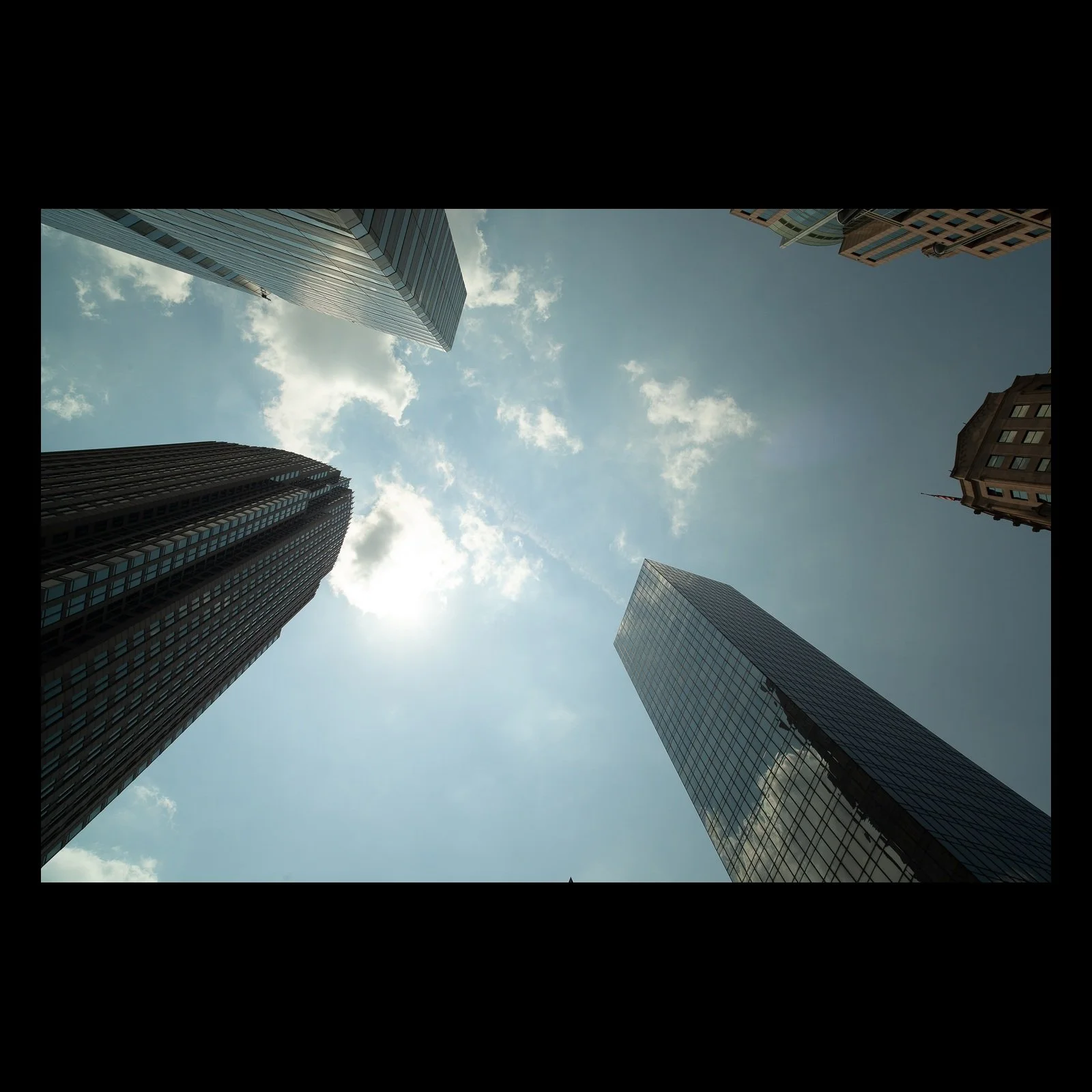 Full-frame black presentation thumbnail of Vertical Weather, showing tall city buildings rise from every edge toward a bright opening of sky