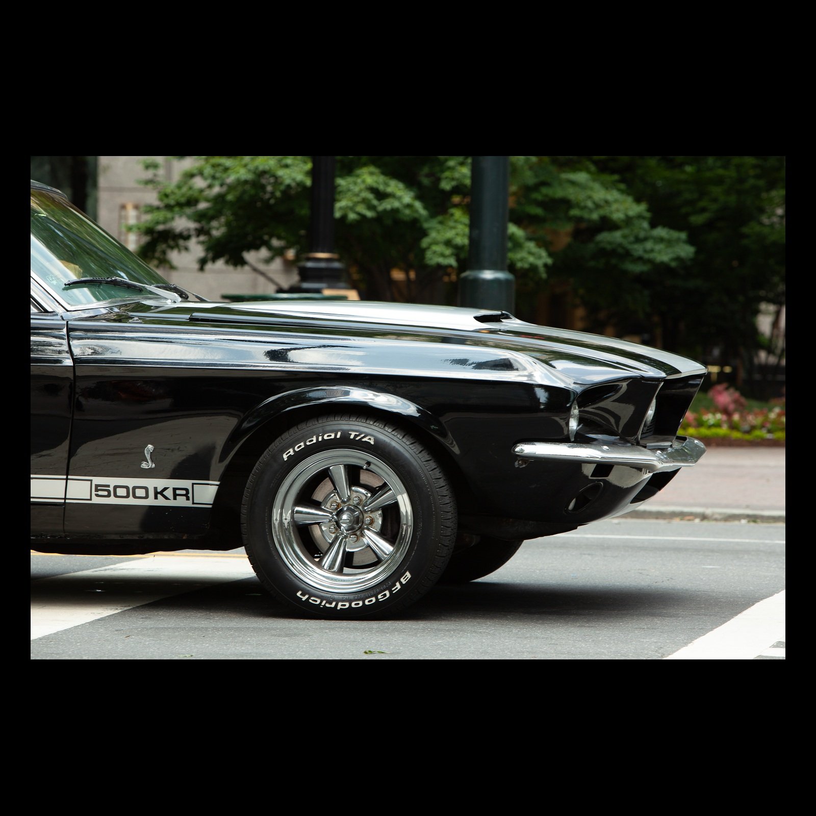 Full-frame black presentation thumbnail of Five Hundred Horses, showing the chrome nose and front wheel of a classic muscle car cut across a city street