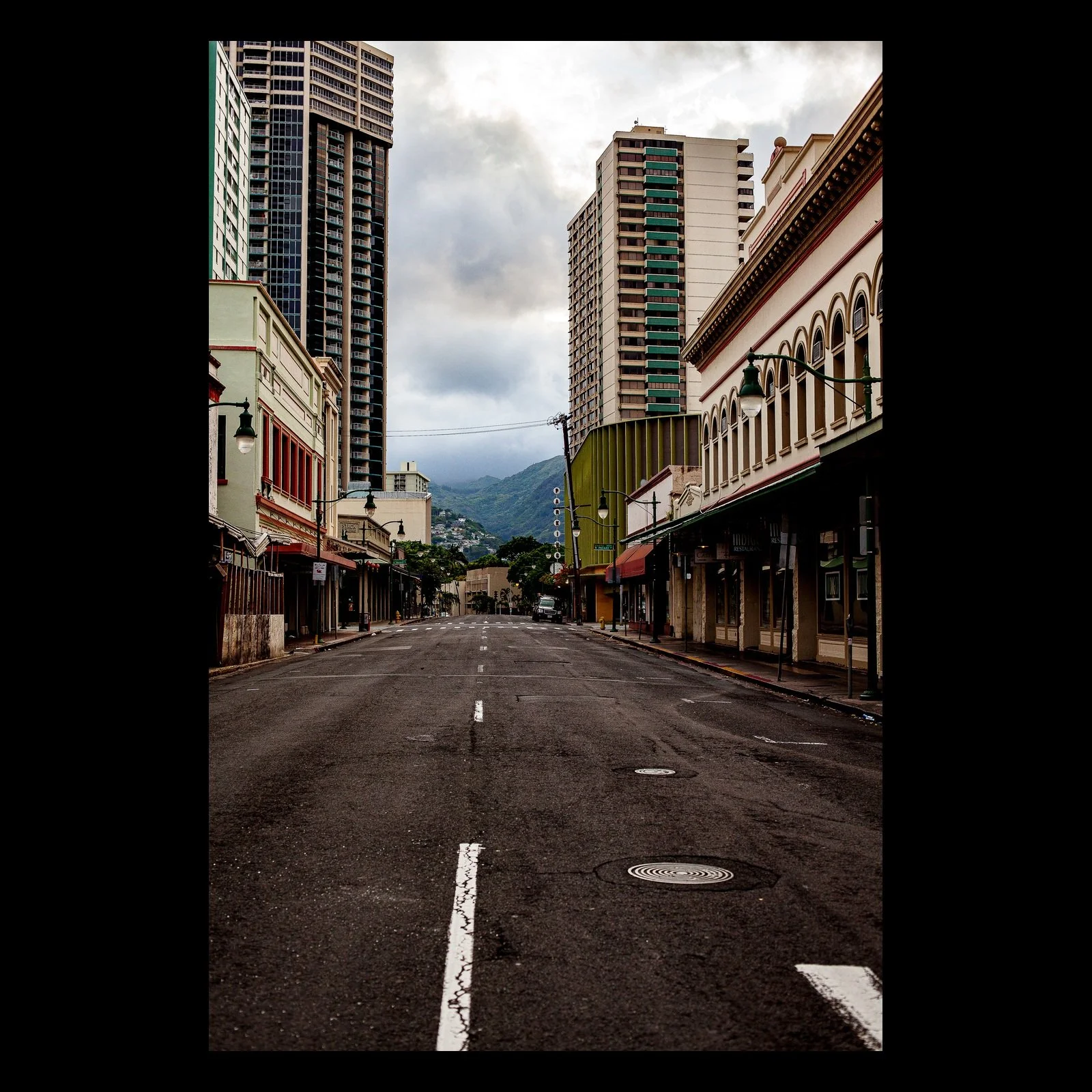 Full-frame black presentation thumbnail of Empty Avenue, showing an empty urban street leads between older storefronts and modern towers toward distant mountains