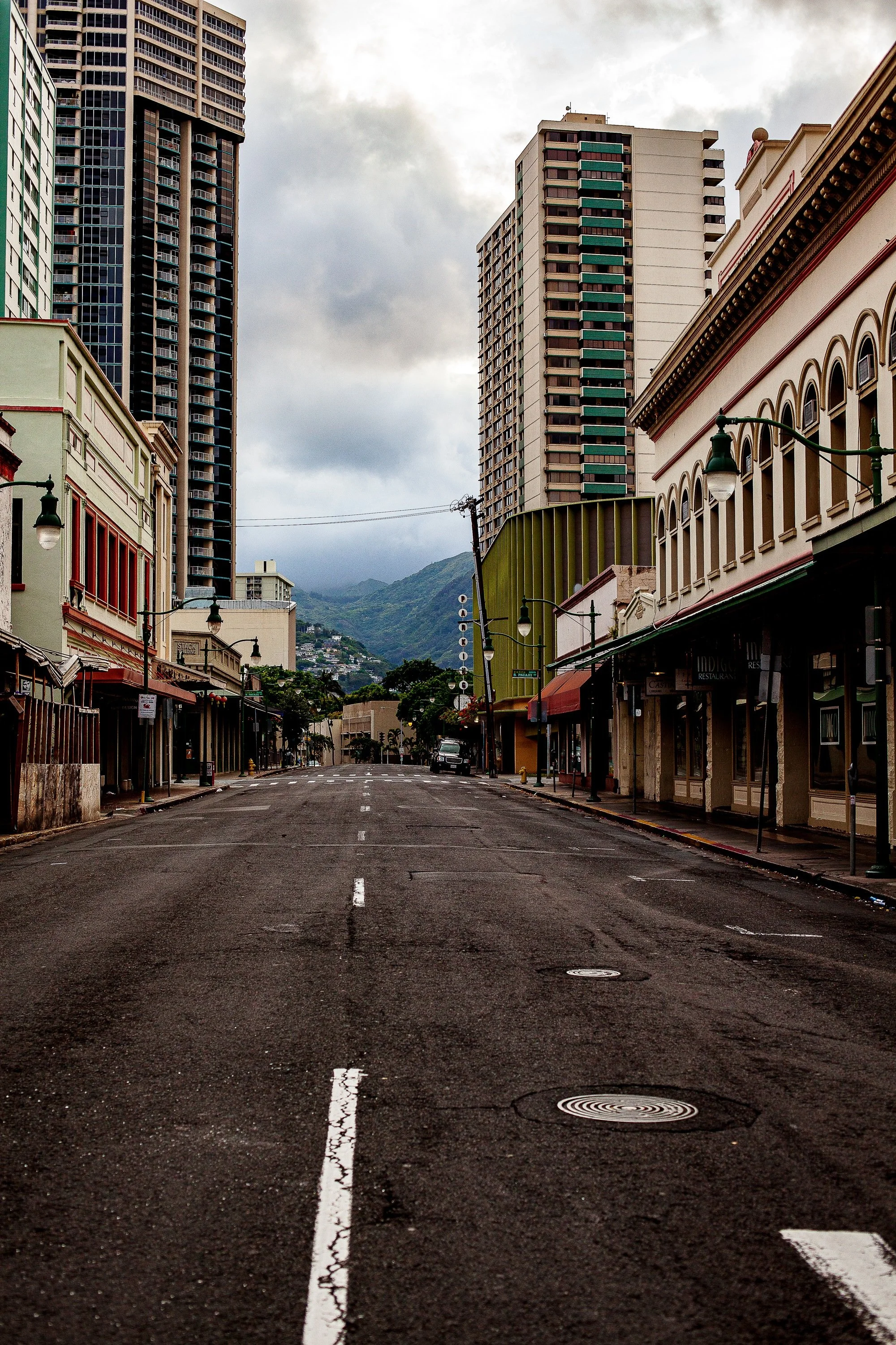 Complete uncropped artwork for Empty Avenue, showing an empty urban street leads between older storefronts and modern towers toward distant mountains