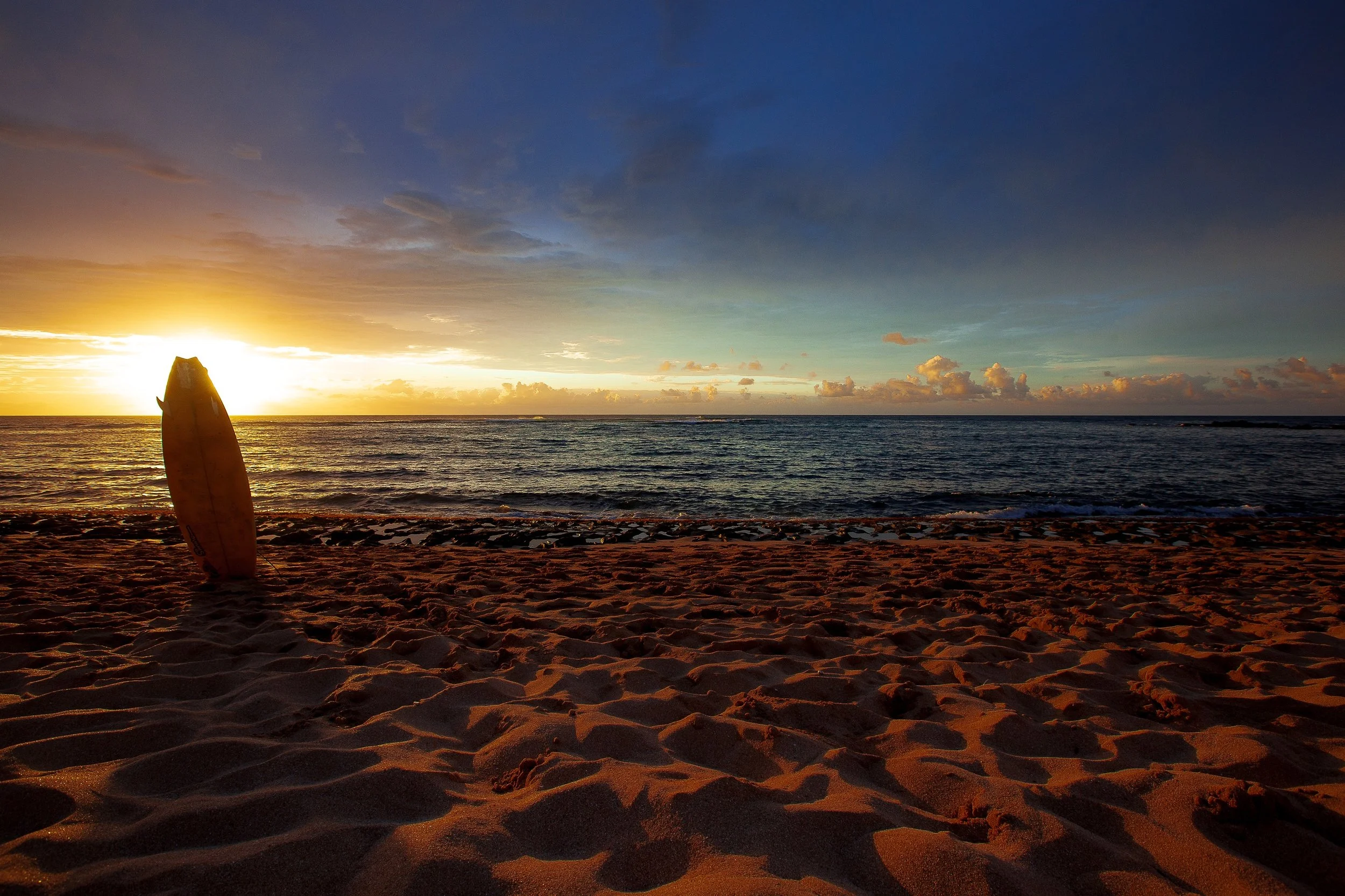 Complete uncropped artwork for Last Board Out, showing a surfboard stands upright in textured sand while the sun drops toward the ocean