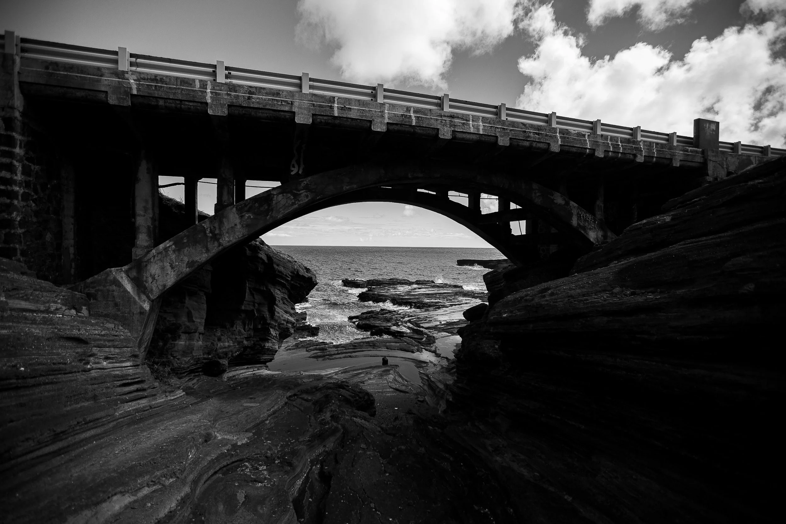 Complete uncropped artwork for Concrete Tide, showing a heavy arched bridge spans dark coastal rock and a narrow view of the sea in black and white
