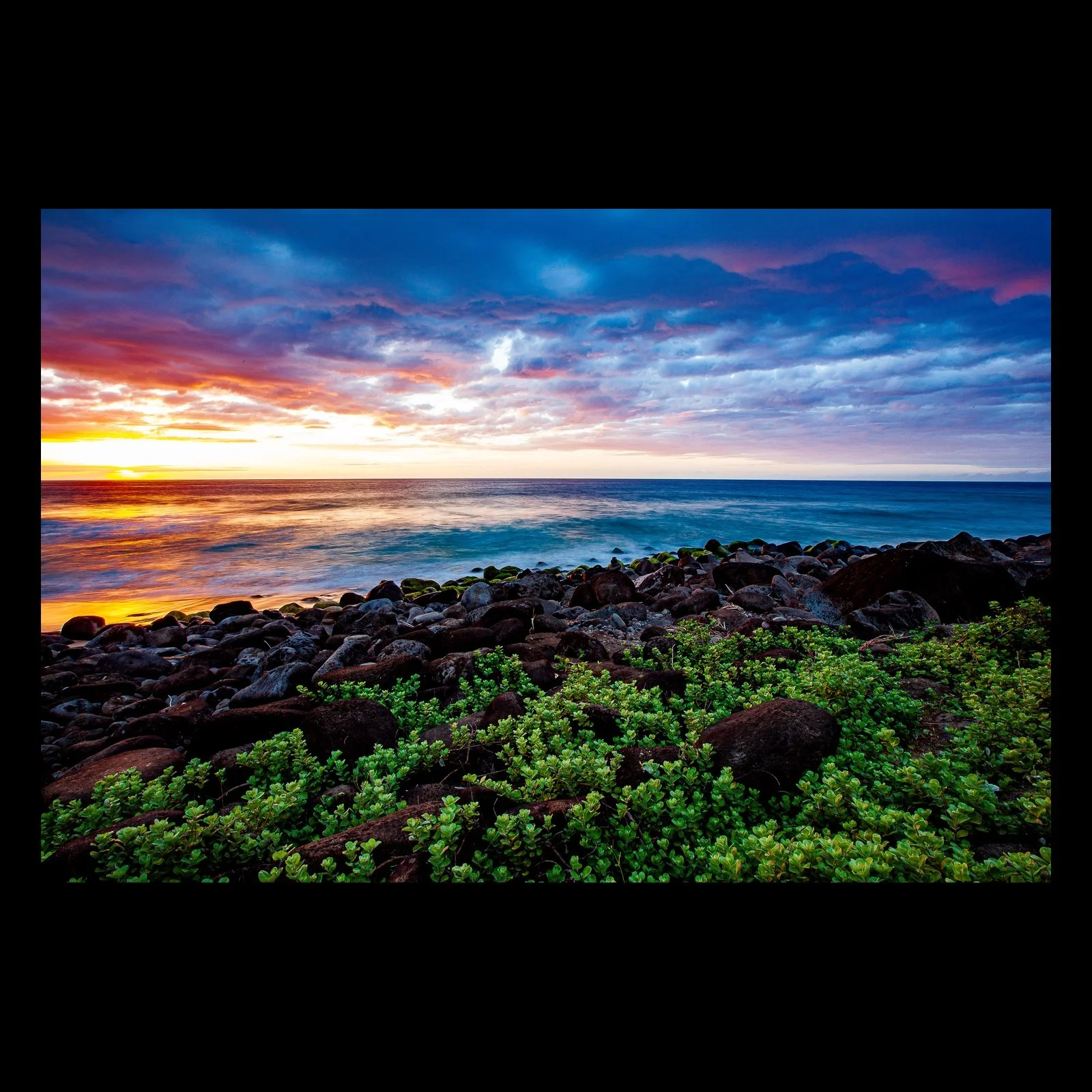 Full-frame black presentation thumbnail of Edge of Color, showing a vivid sunset settles over dark coastal rocks and dense green shoreline plants