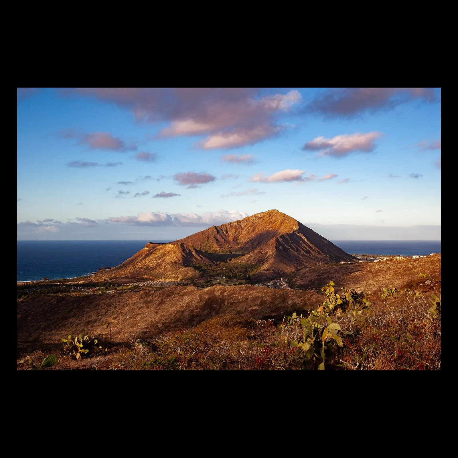 Full-frame black presentation thumbnail of Crater in Morning Light, showing a weathered volcanic crater rises from rust-colored ground beneath blue sky and pink clouds
