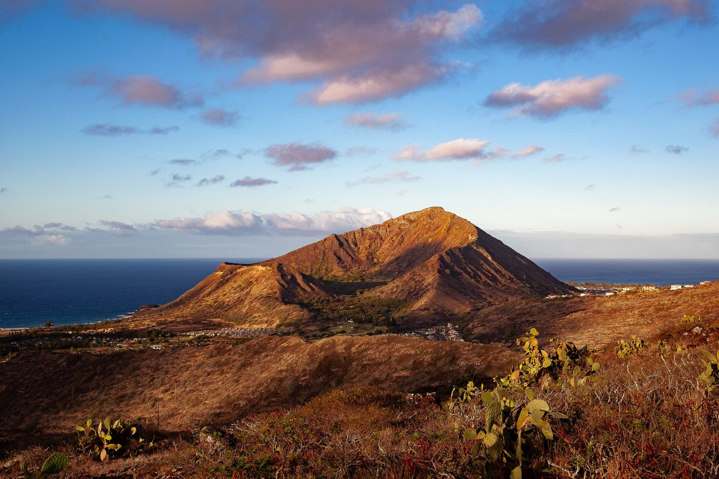 Complete uncropped artwork for Crater in Morning Light, showing a weathered volcanic crater rises from rust-colored ground beneath blue sky and pink clouds
