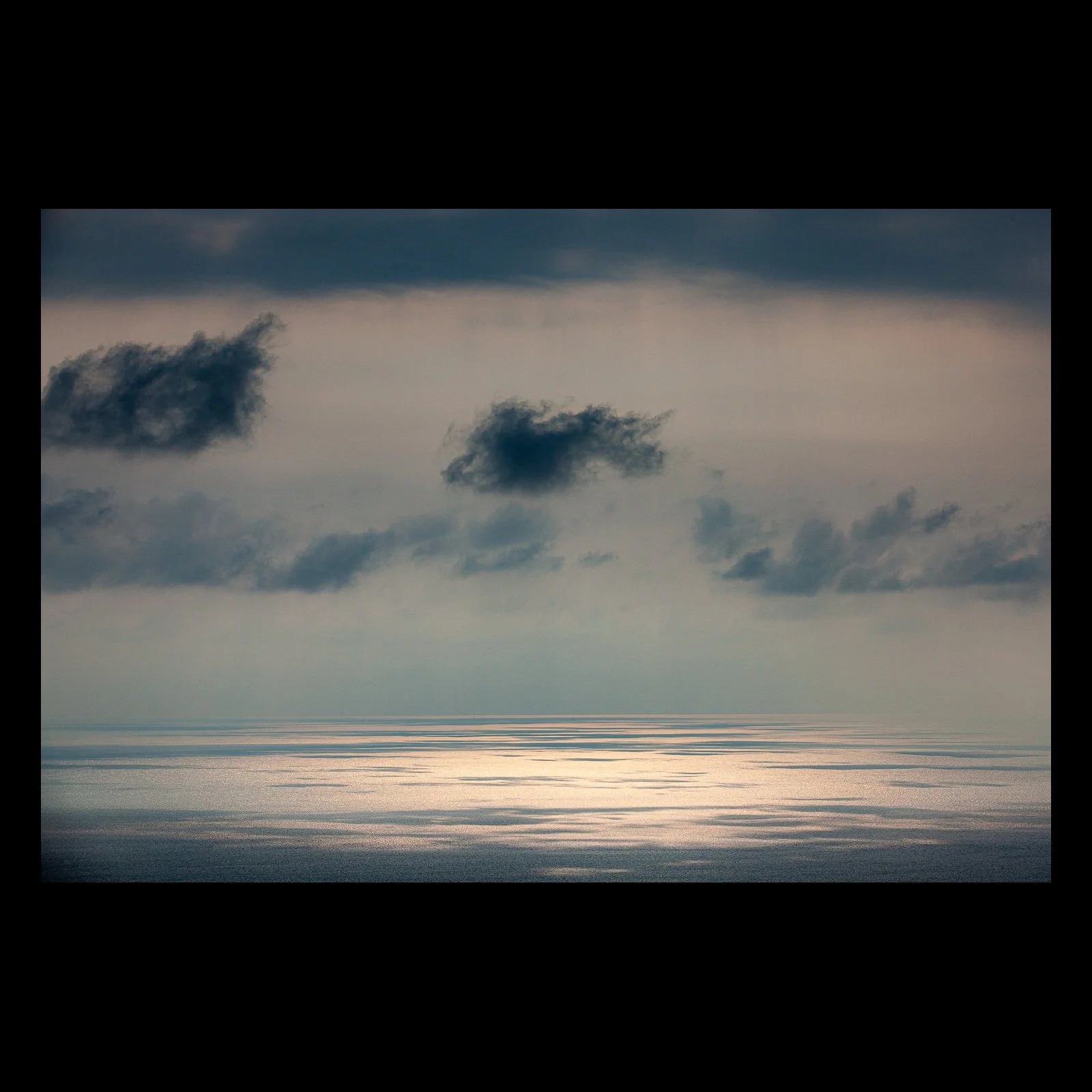 Full-frame black presentation thumbnail of Silver Water, showing a pale opening in the clouds reflects as a silver band across a subdued ocean