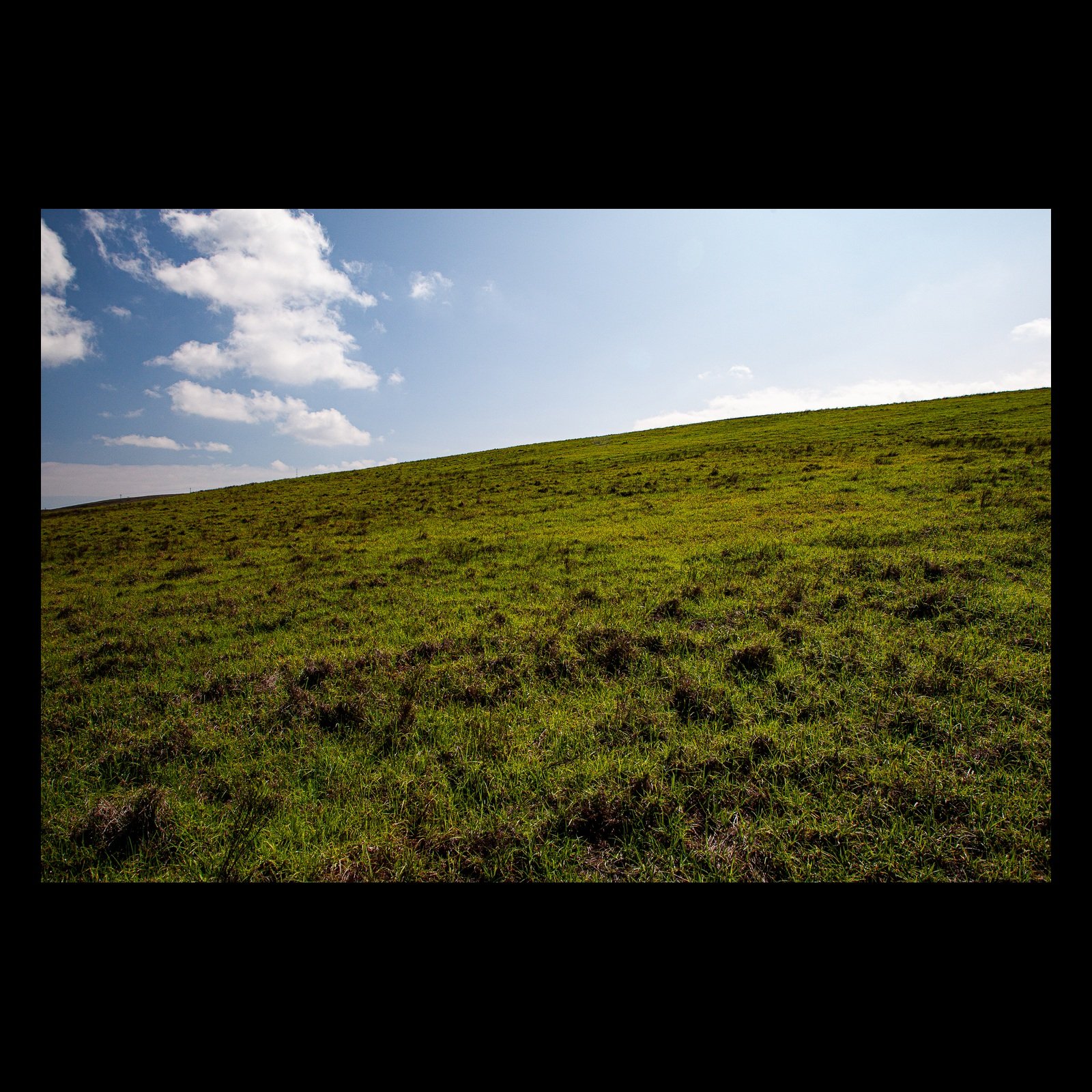 Full-frame black presentation thumbnail of The Green Incline, showing a simple grassy slope rises diagonally beneath an open sky with scattered clouds