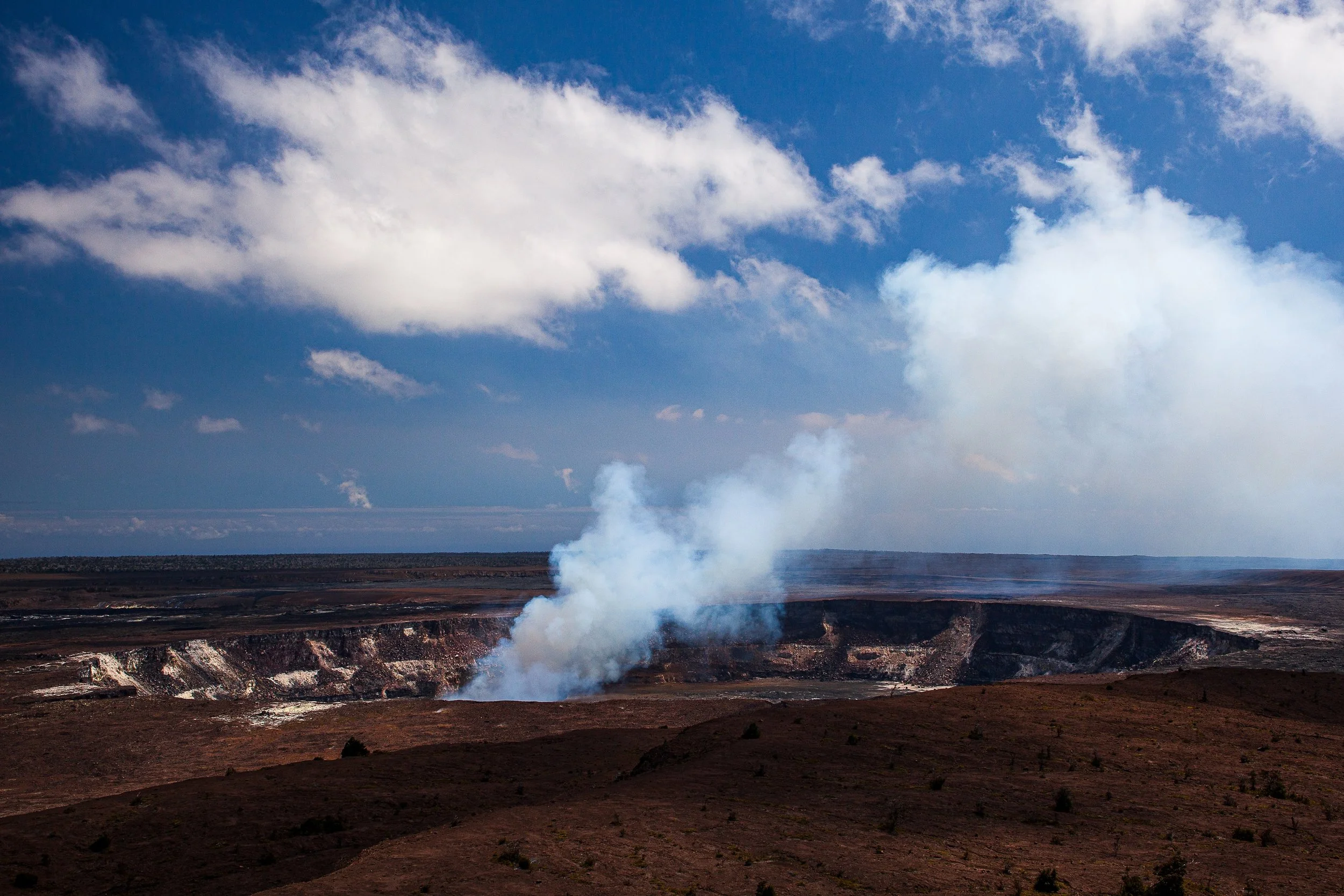 Complete uncropped artwork for Earth Breathing, showing white steam rises from a broad volcanic crater beneath bright clouds and blue sky