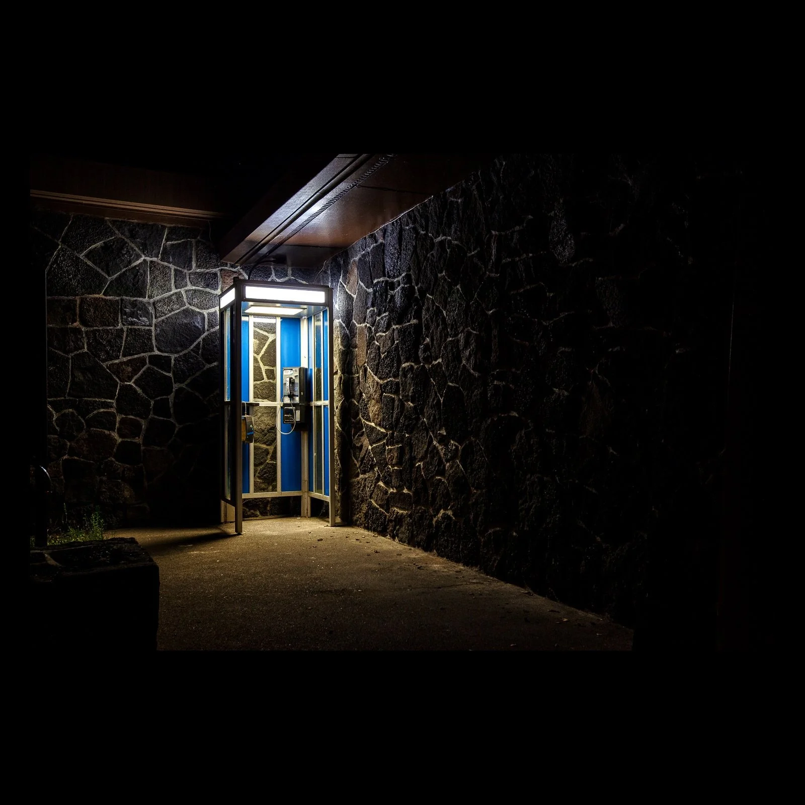 Full-frame black presentation thumbnail of Open After Dark, showing a bright glass doorway opens from a dark wall of rough volcanic stone