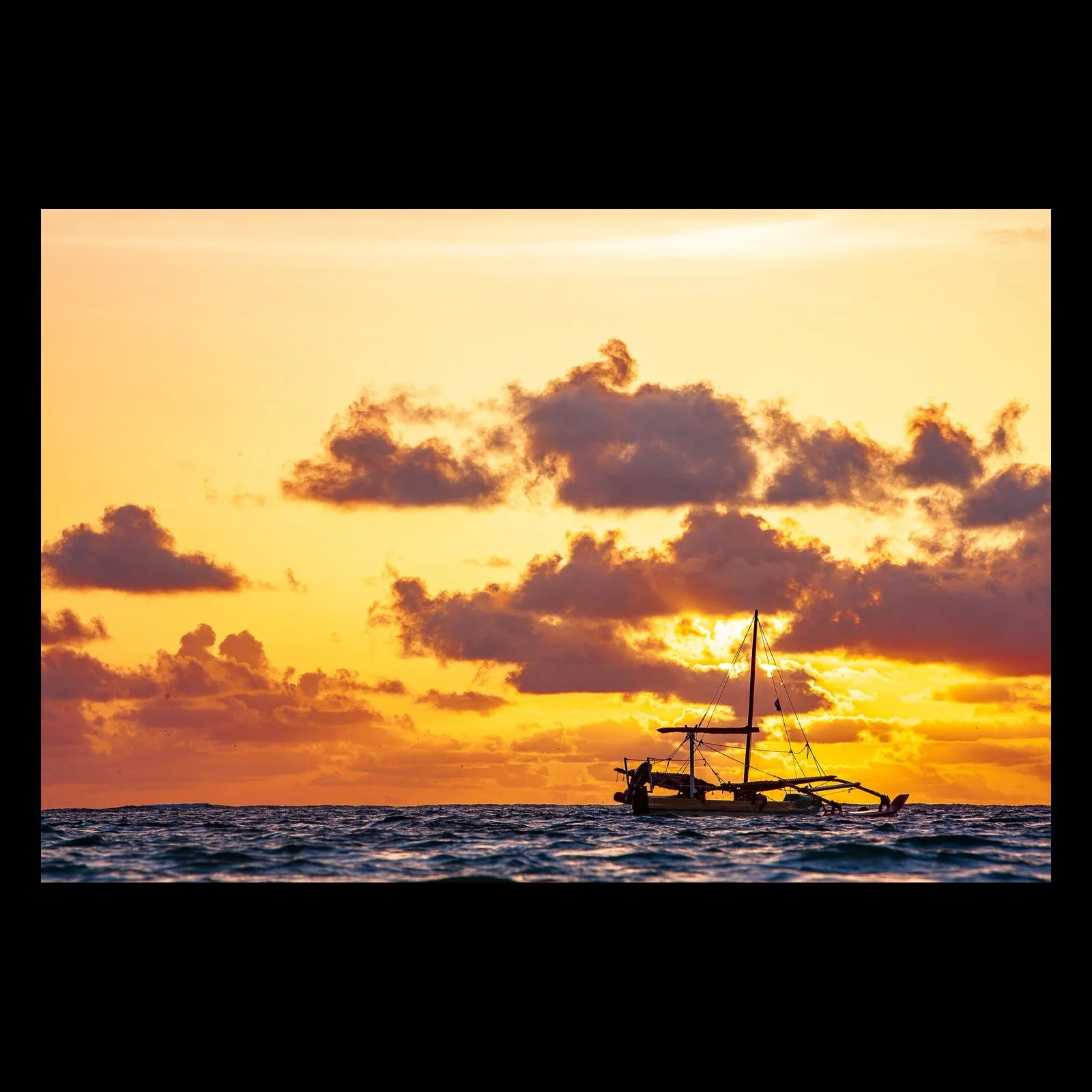 Full-frame black presentation thumbnail of Outrigger Evening, showing an outrigger boat rides low on dark waves beneath an orange cloud-filled sunset