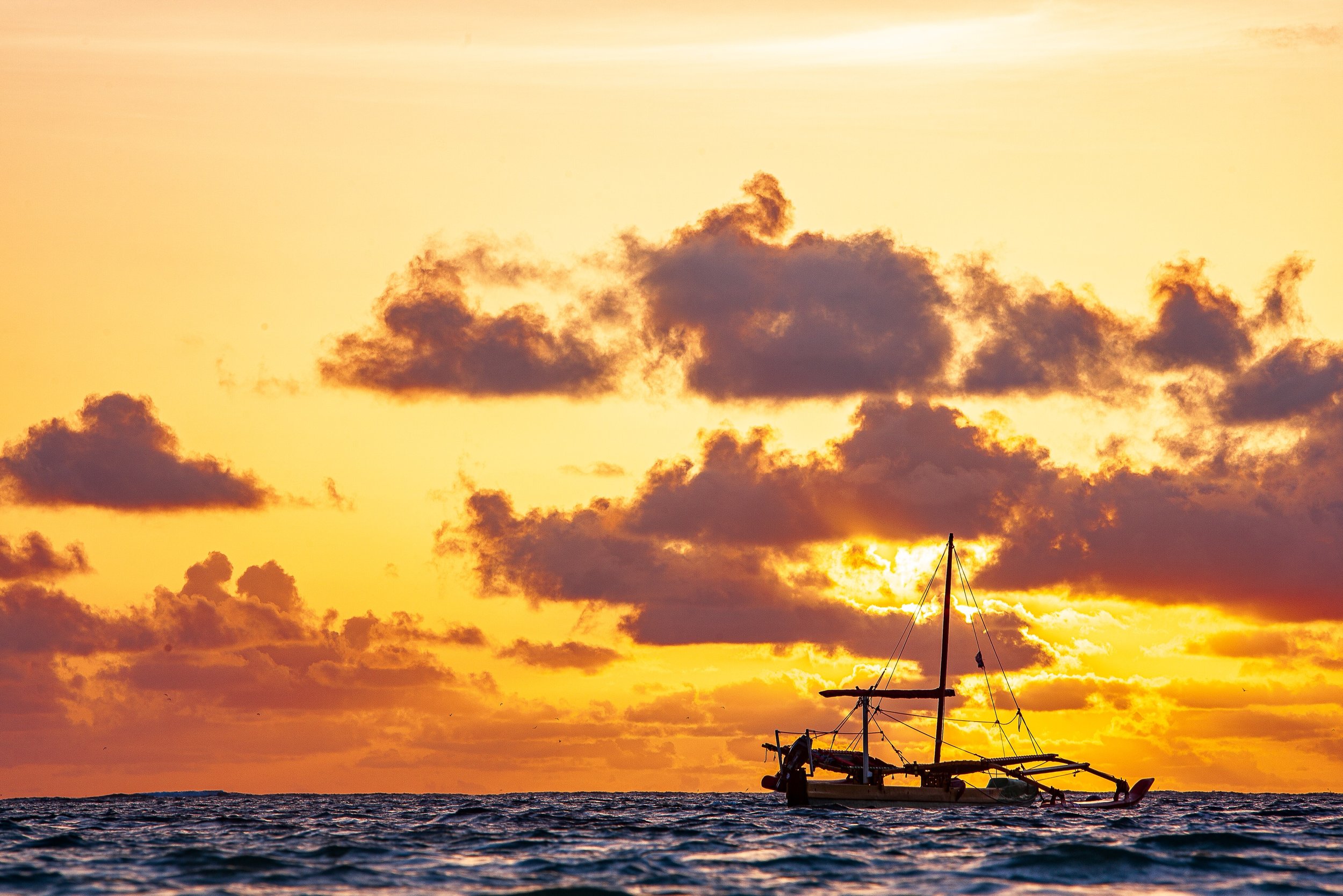 Complete uncropped artwork for Outrigger Evening, showing an outrigger boat rides low on dark waves beneath an orange cloud-filled sunset