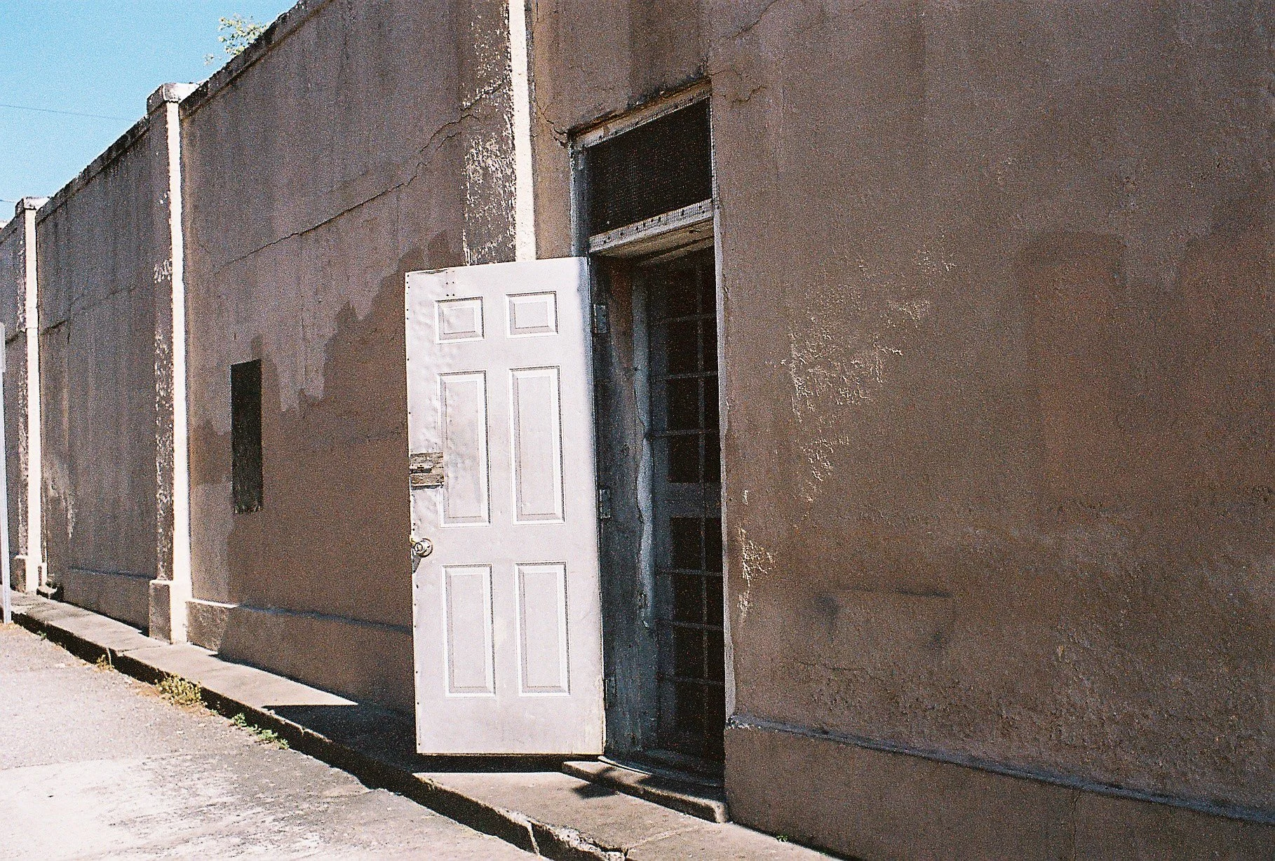 Complete uncropped artwork for The Open Door, showing a white door stands open in a sunlit wall marked by age and peeling surfaces
