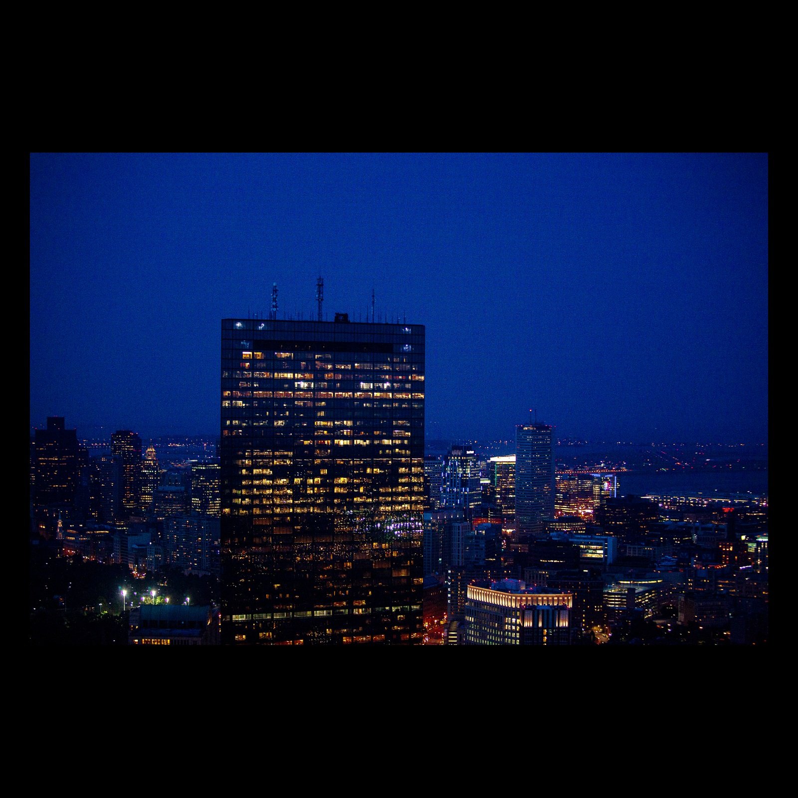 Full-frame black presentation thumbnail of One Building Awake, showing a dark glass tower glows with scattered office lights against a deep blue city night