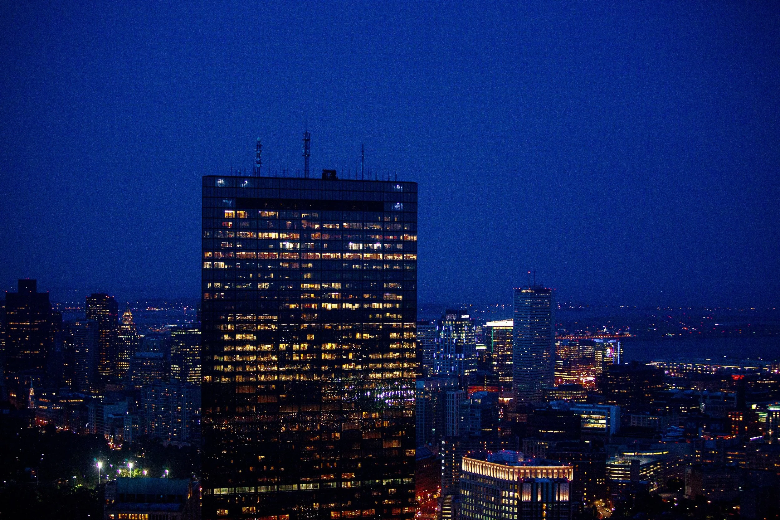 Complete uncropped artwork for One Building Awake, showing a dark glass tower glows with scattered office lights against a deep blue city night
