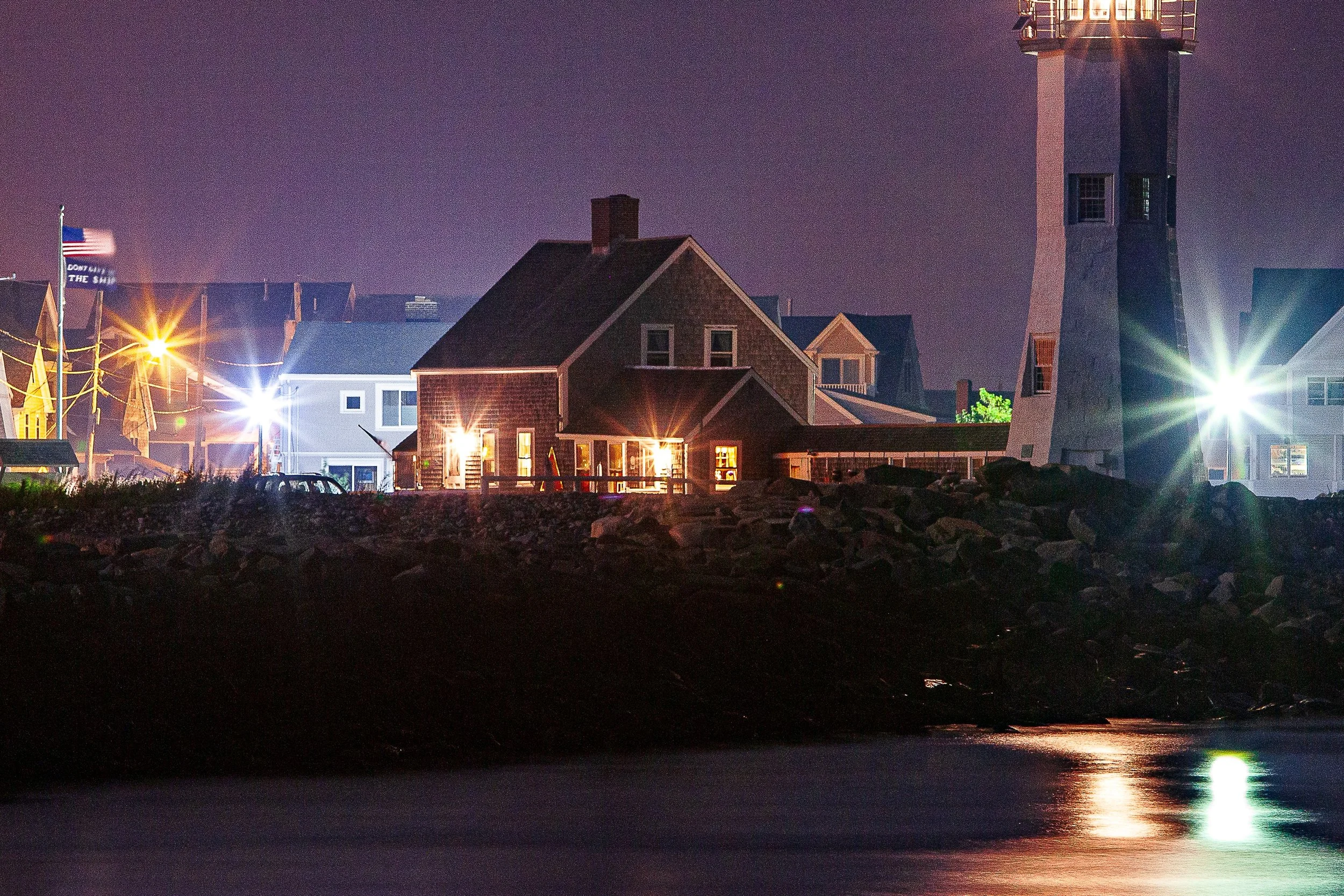 Detail crop from Harbor Lantern, emphasizing small points of window light reveal the settlement around the stronger beacon