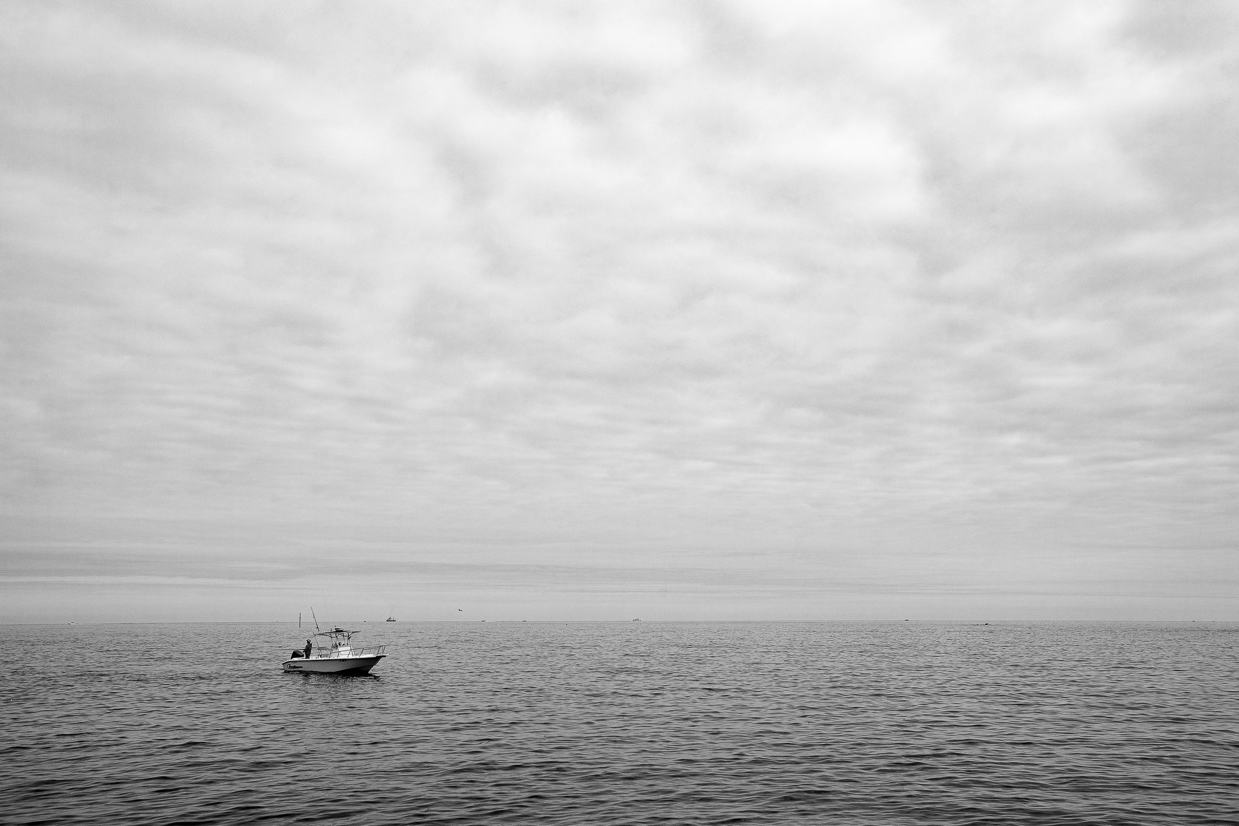 Complete uncropped artwork for A Boat in the Blank, showing a single small boat rests beneath an expansive gray sky and faint horizon in black and white