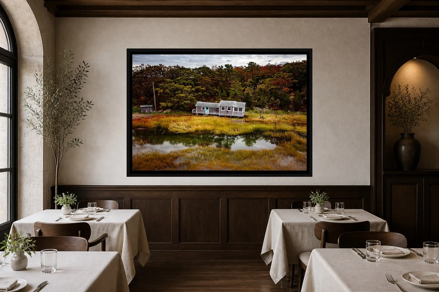 Salt Marsh Quiet displayed in a black frame within an intimate fine-dining room with plaster walls, dark wood, linen tables, no guests, and a clear central wall