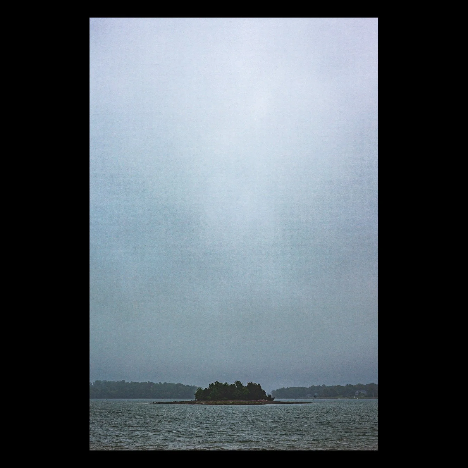 Full-frame black presentation thumbnail of Rain Between Shores, showing a distant island appears beneath a vertical veil of rain in a cool-toned seascape