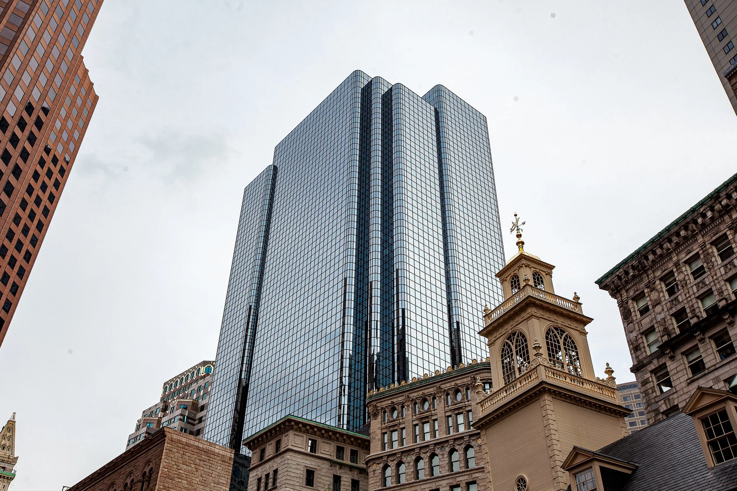 Complete uncropped artwork for Old and New, showing a reflective modern tower rises between older stone and brick buildings in a low-angle city view