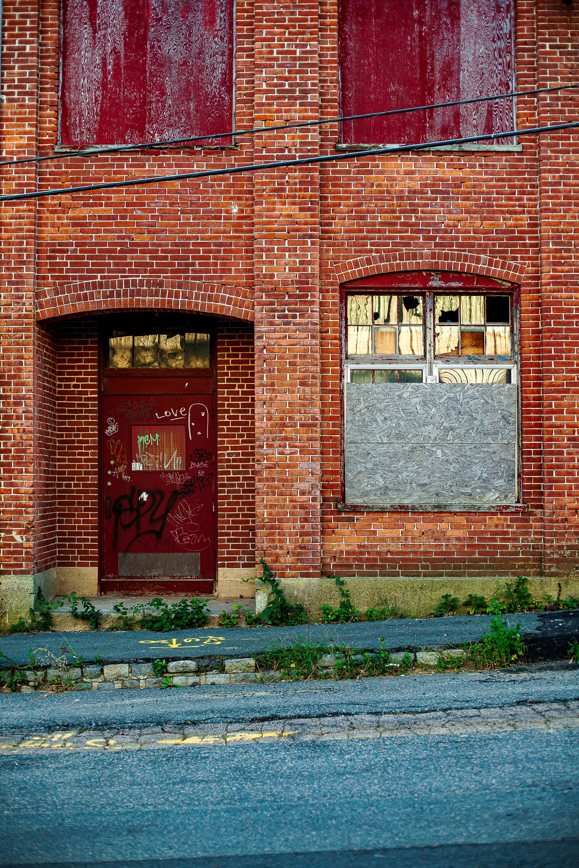 Complete uncropped artwork for Tainted Love, showing a red door and boarded window punctuate an aging brick facade
