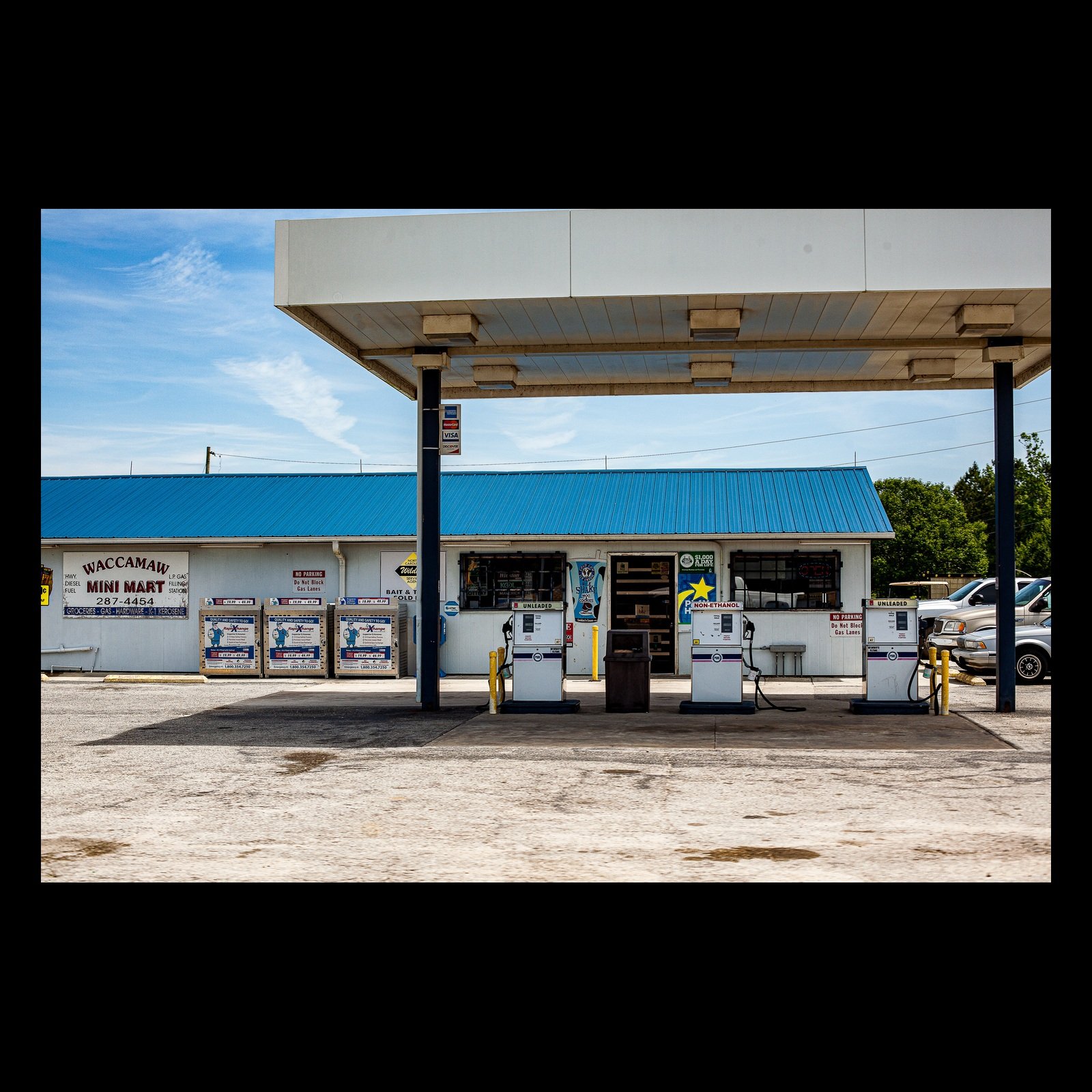 Full-frame black presentation thumbnail of Last Fuel, showing a modest roadside gas station sits beneath a bright blue roof and open sky