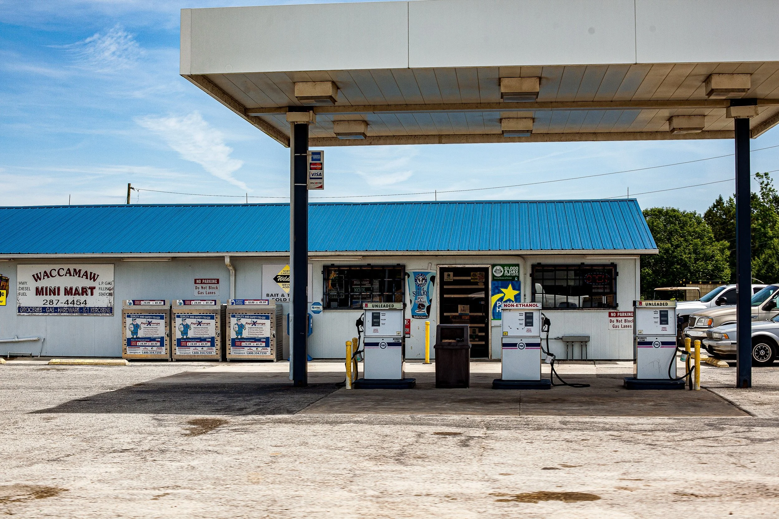 Complete uncropped artwork for Last Fuel, showing a modest roadside gas station sits beneath a bright blue roof and open sky