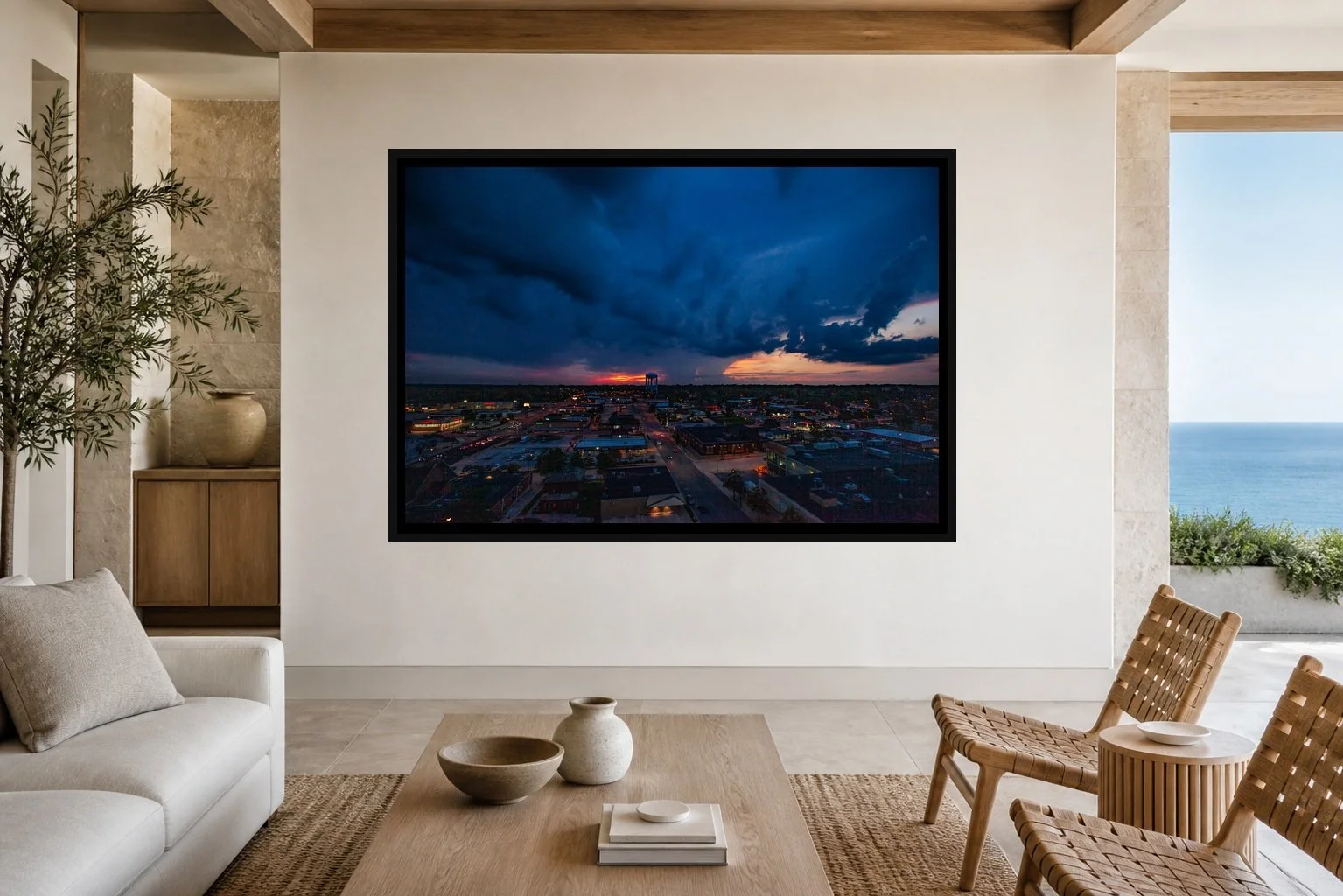 Storm Over Town displayed in a black frame within a restrained coastal residence with pale stone, white oak, woven seating, and a clear central wall