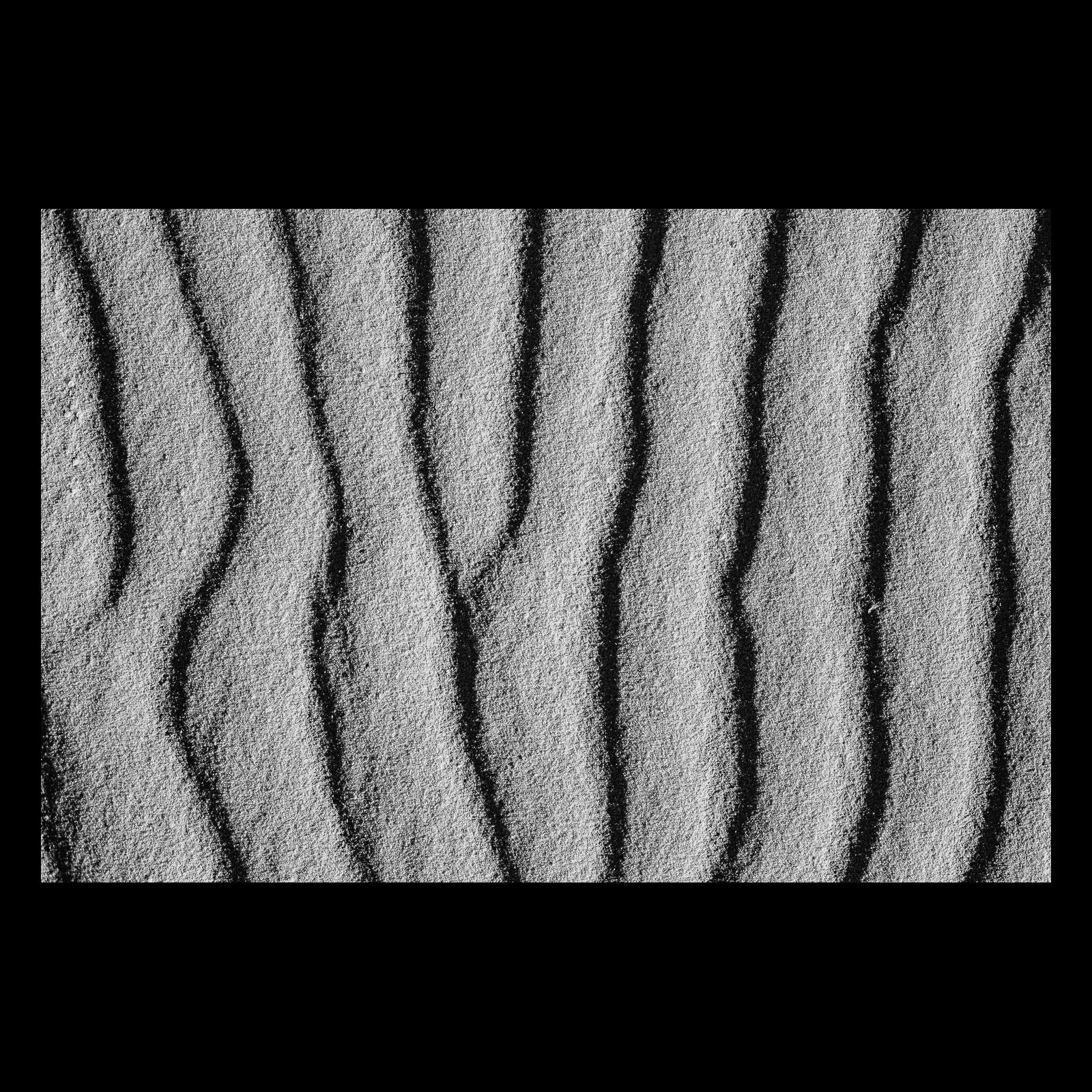 Full-frame black presentation thumbnail of Wind Written, showing fine parallel ridges run through pale sand in a tightly framed monochrome study