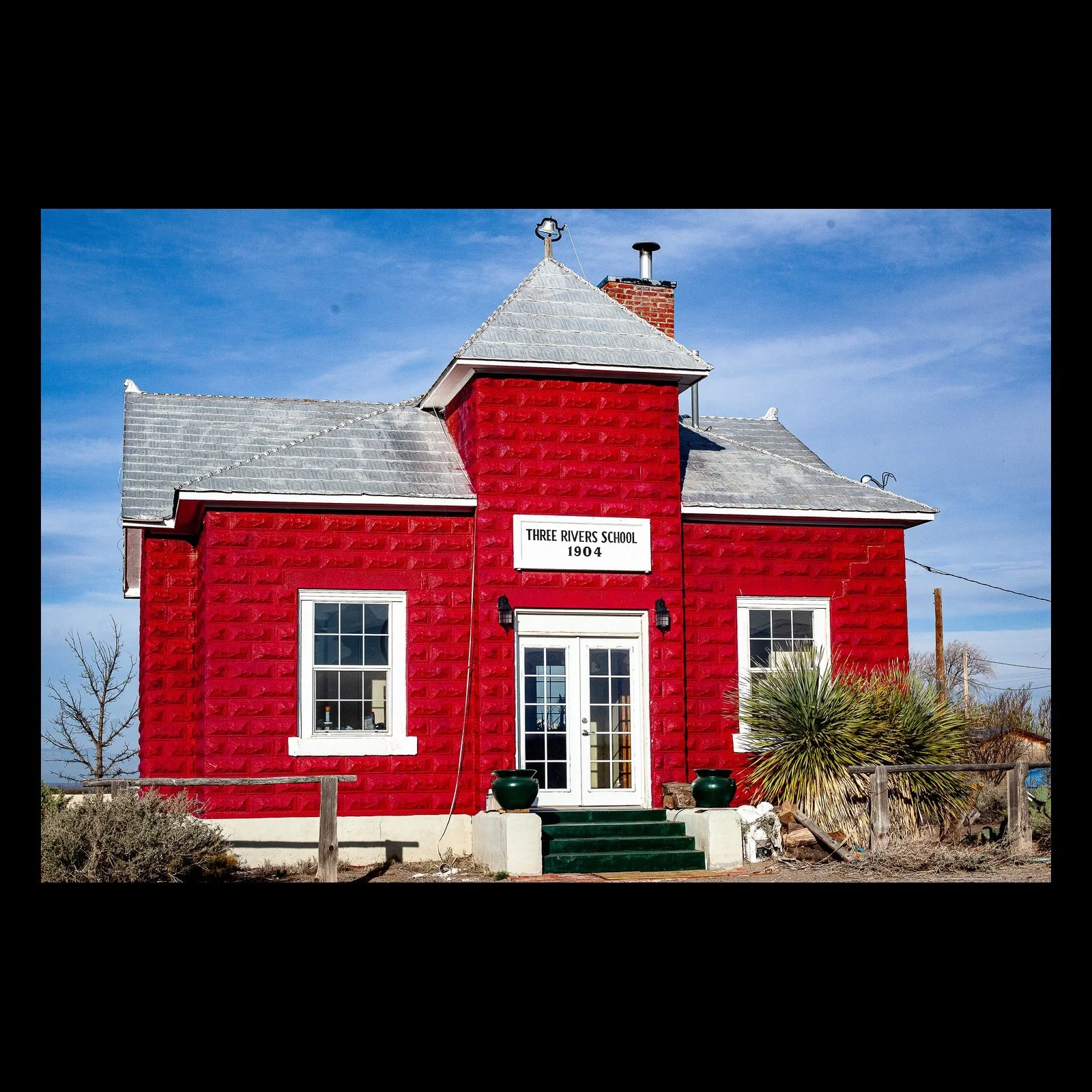 Full-frame black presentation thumbnail of The Red Schoolhouse, showing a bright red historic schoolhouse stands alone beneath a blue sky