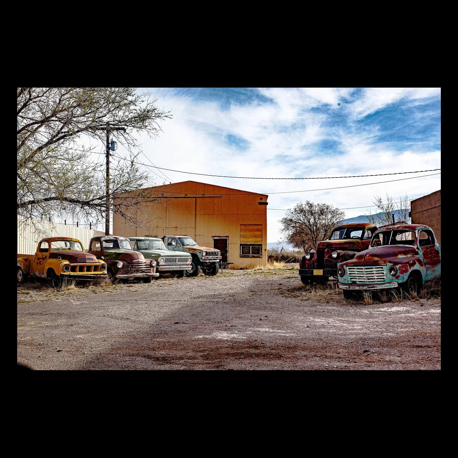 Full-frame black presentation thumbnail of Working Relics, showing a row of weathered trucks waits outside an industrial building under winter light