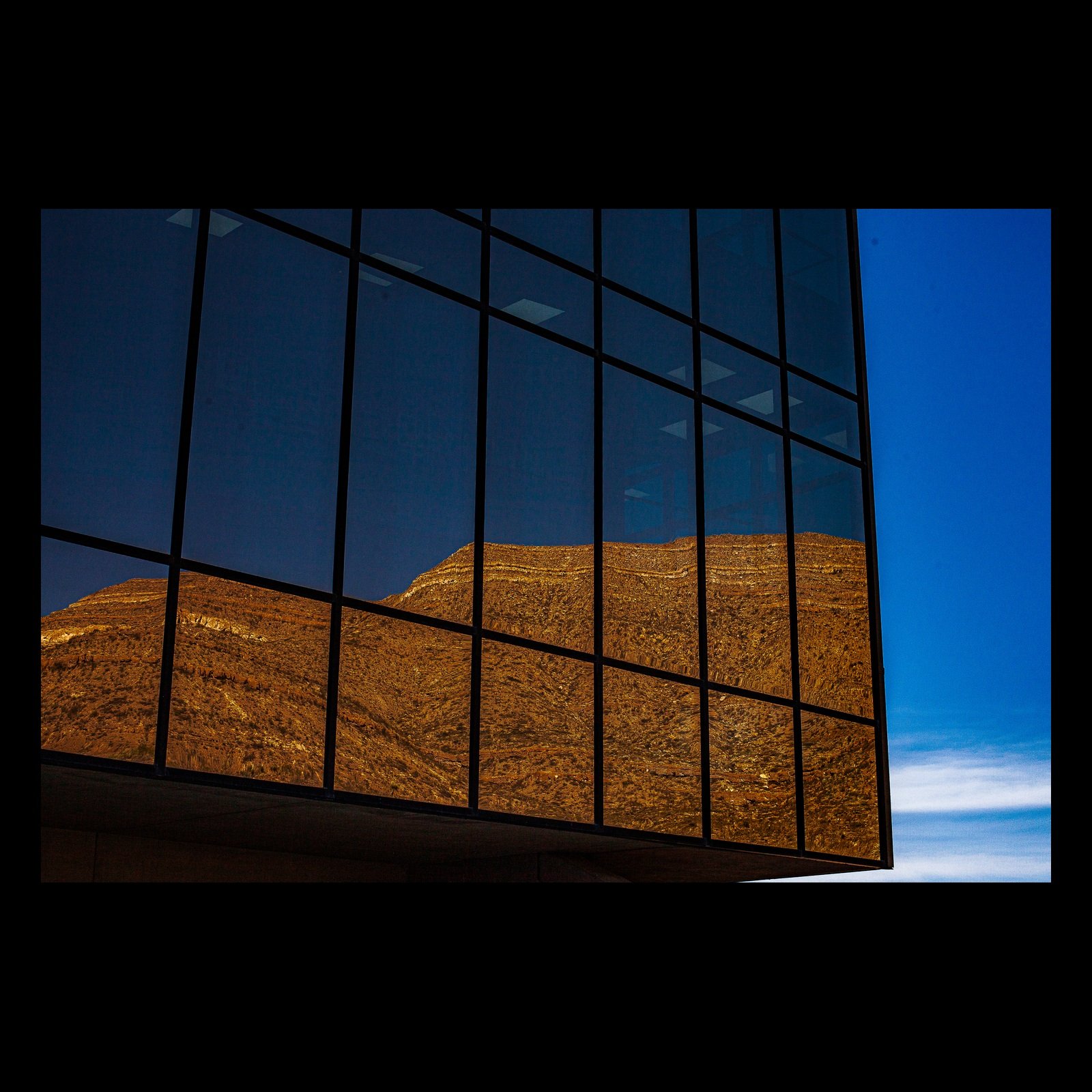 Full-frame black presentation thumbnail of Borrowed Mountain, showing a golden mountain appears as a reflection across a grid of dark glass
