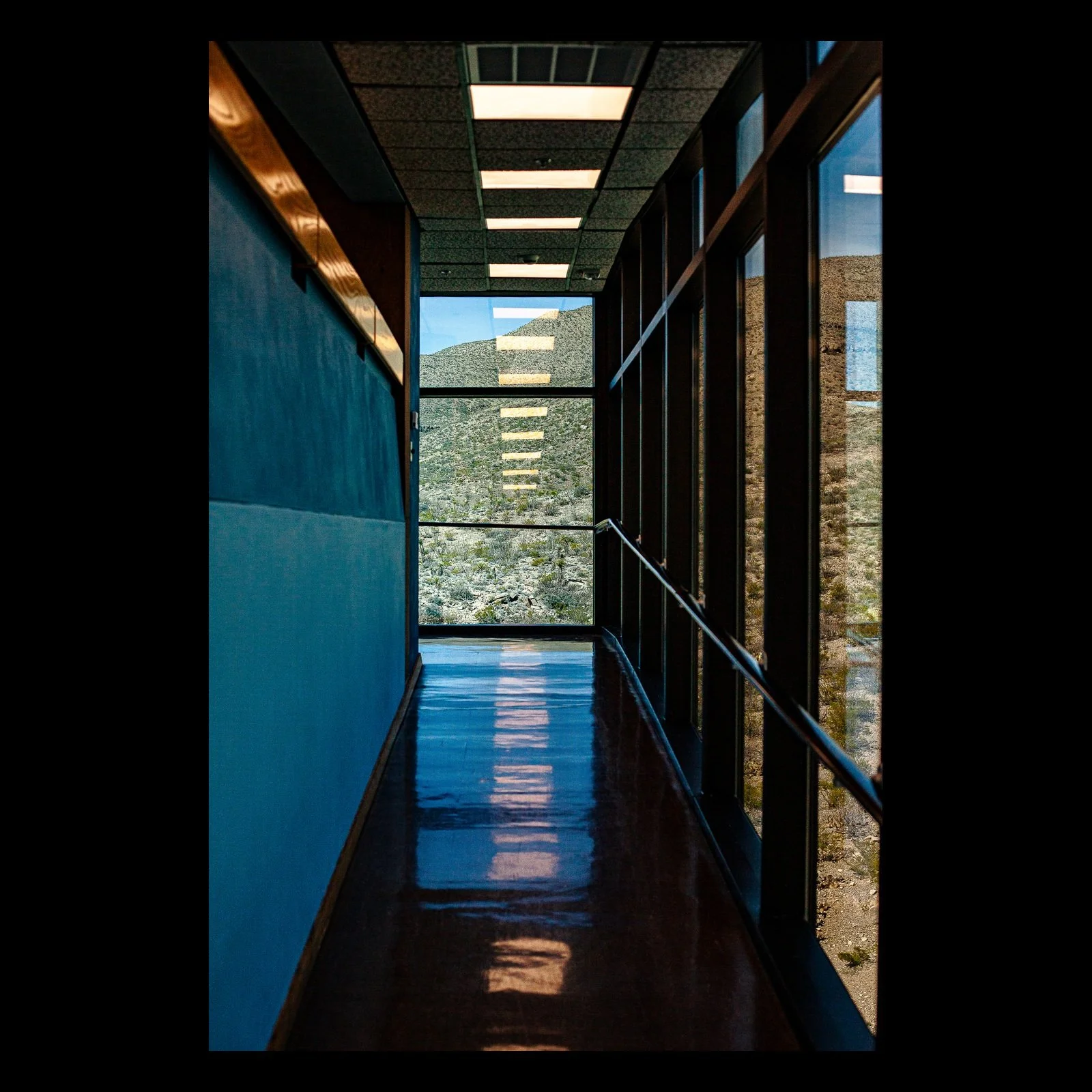 Full-frame black presentation thumbnail of Corridor in Blue, showing a narrow blue corridor leads through repeating windows toward a bright exterior opening