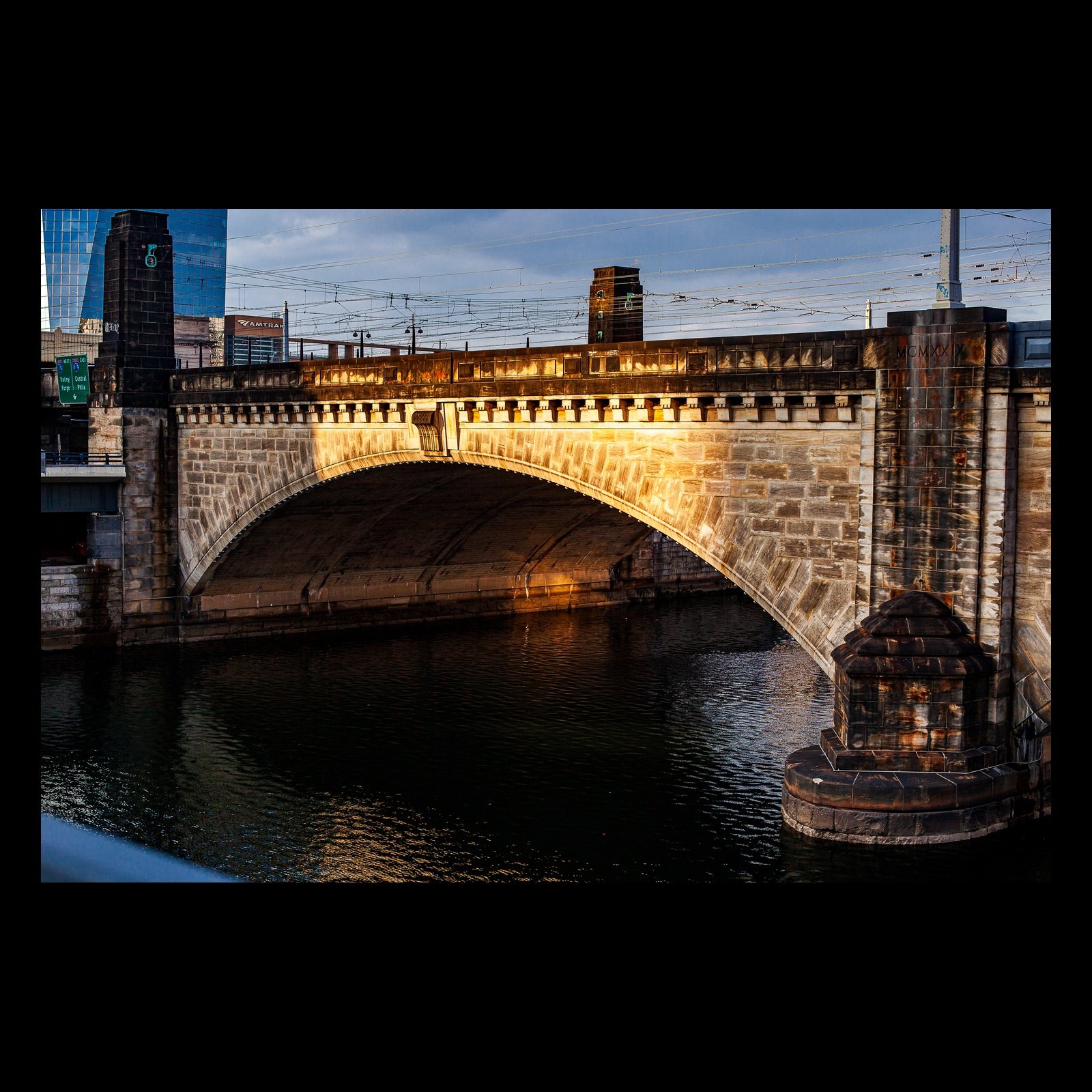 Full-frame black presentation thumbnail of Stone Crossing, showing warm late light traces an old stone bridge reflected in dark river water
