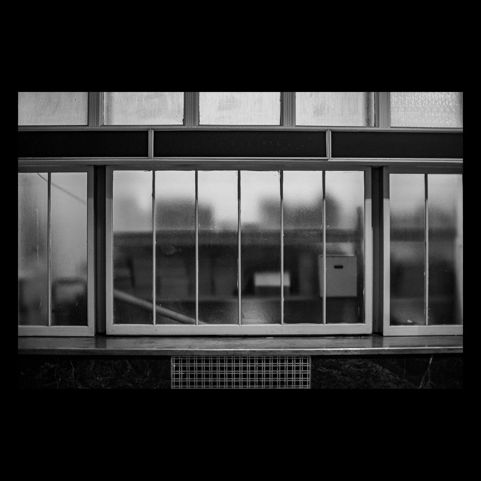 Full-frame black presentation thumbnail of Frosted Interior, showing industrial windows form a black-and-white grid of translucent panes and blurred shapes