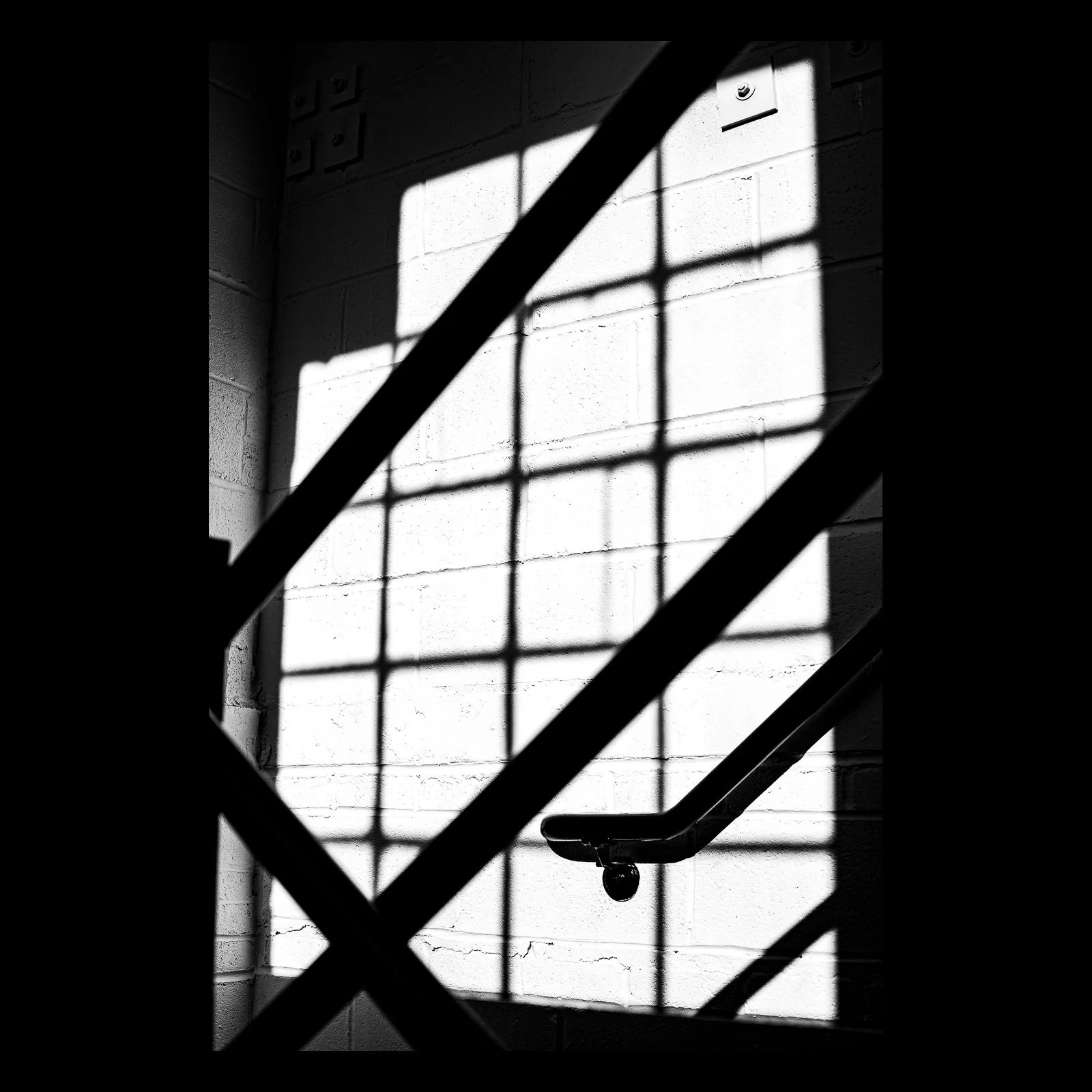 Full-frame black presentation thumbnail of Shadow Rail, showing a diagonal handrail and structural shadows cut across a bright industrial window in black and white
