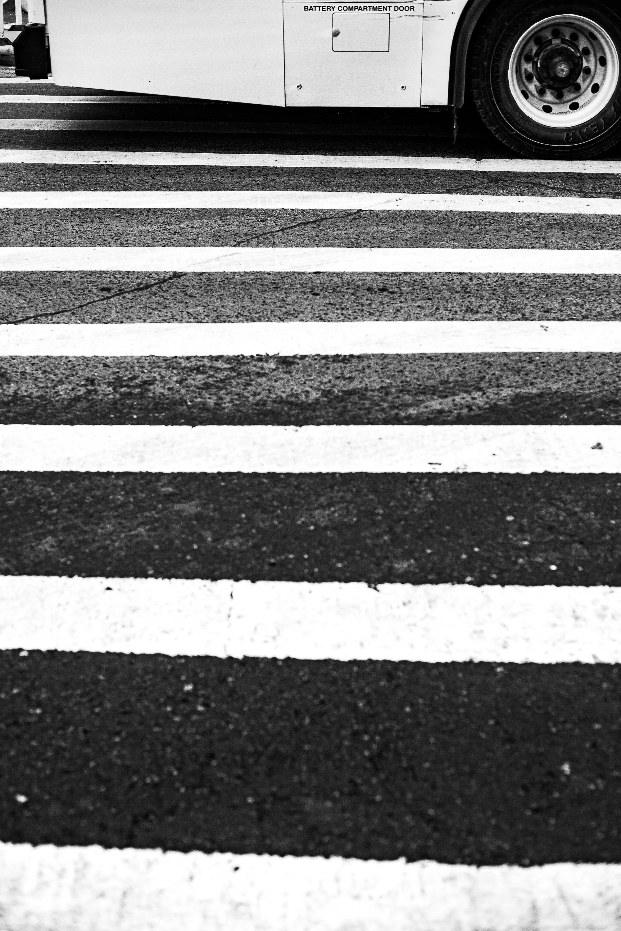 Complete uncropped artwork for Crossing Lines, showing a bus tire meets bold white crosswalk stripes in a narrow vertical street view