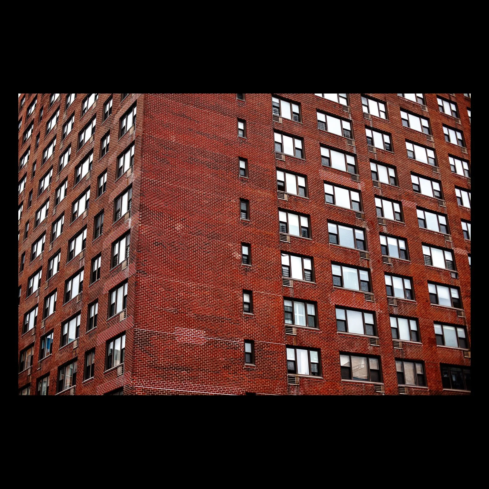 Full-frame black presentation thumbnail of Brick Repetition, showing rows of windows repeat across a tall red-brick residential facade