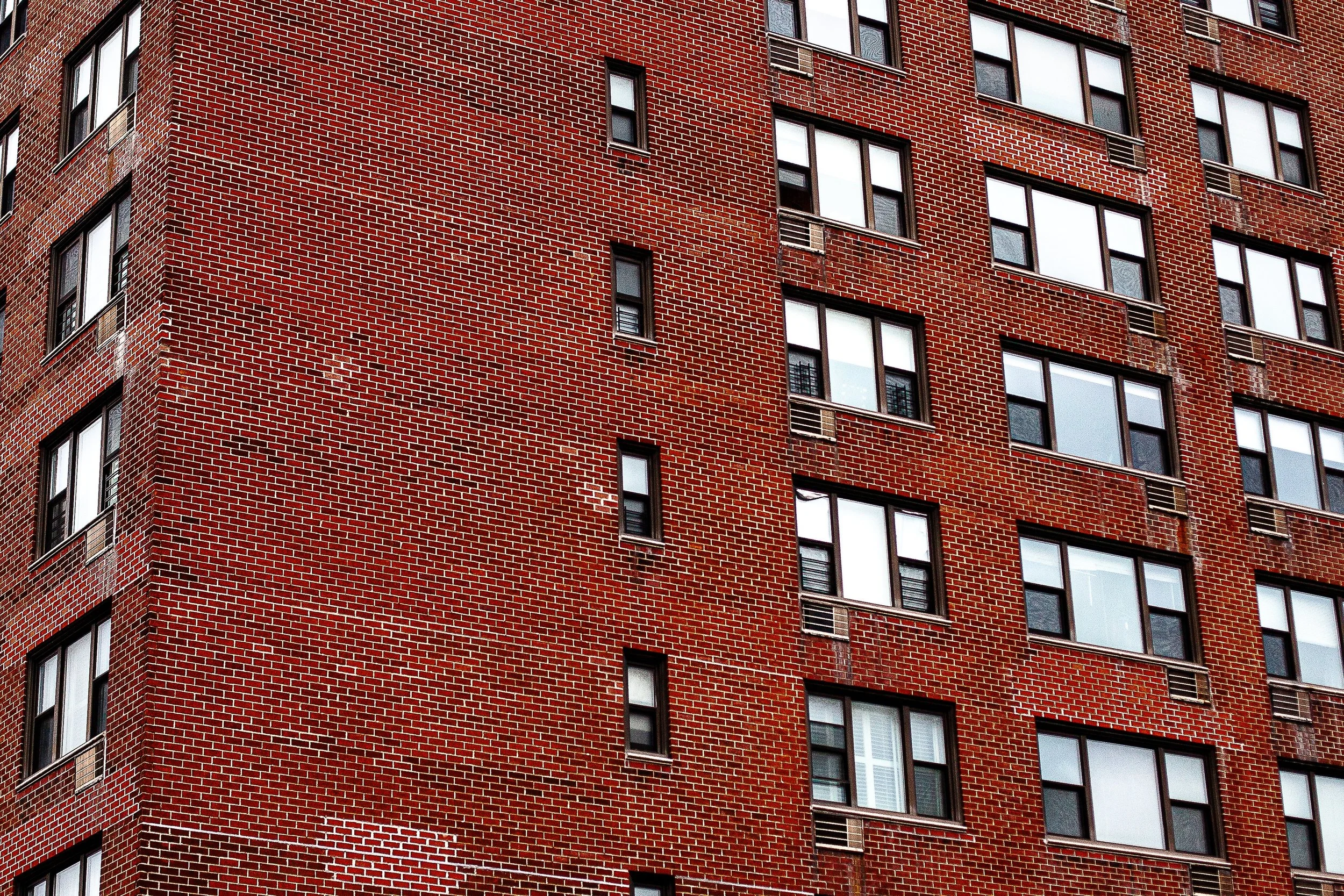 Detail crop from Brick Repetition, emphasizing open shades, darker panes, and repaired brick make individual lives faintly visible