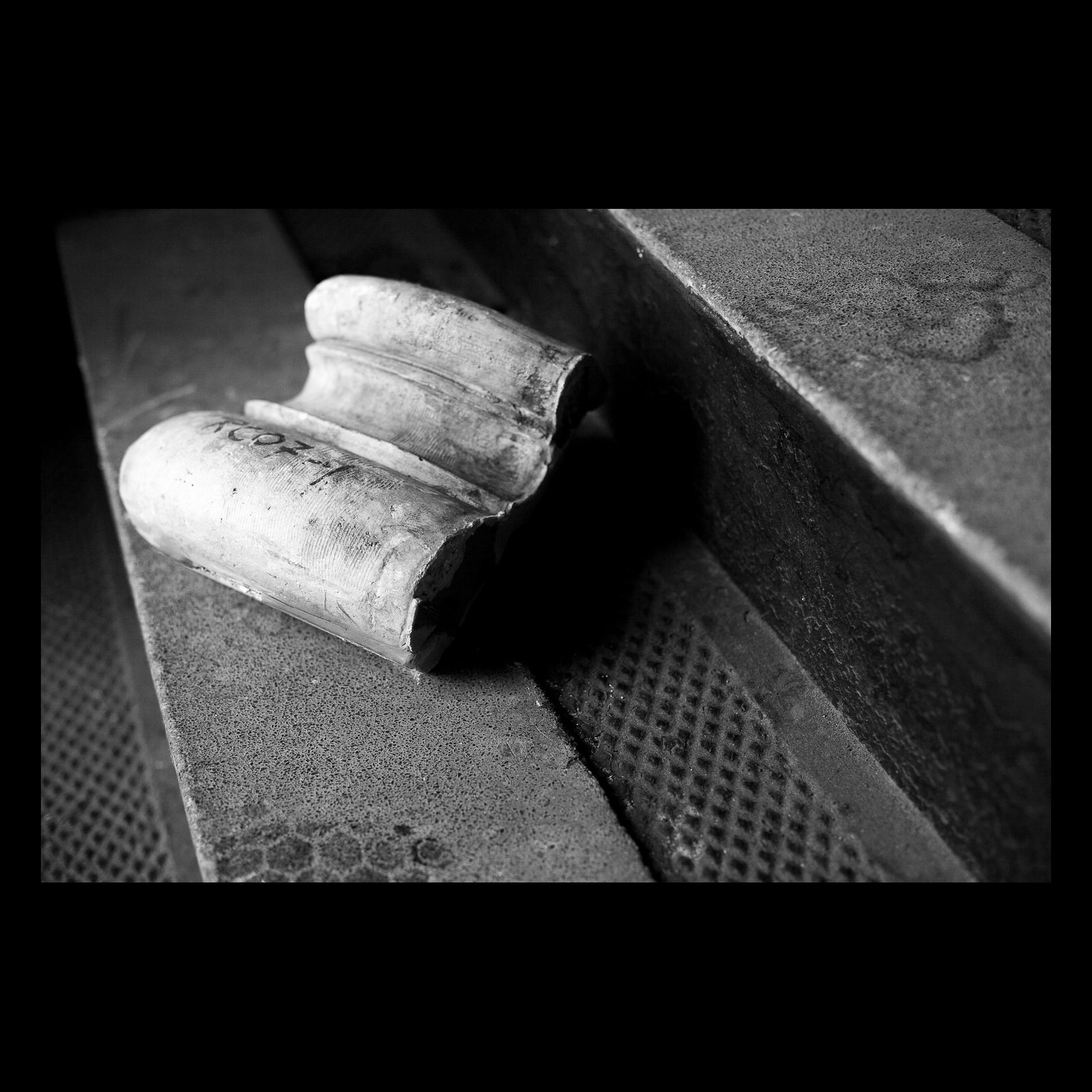 Full-frame black presentation thumbnail of Fallen Fragment, showing a damaged pale architectural fragment rests on a dark industrial ledge in black and white