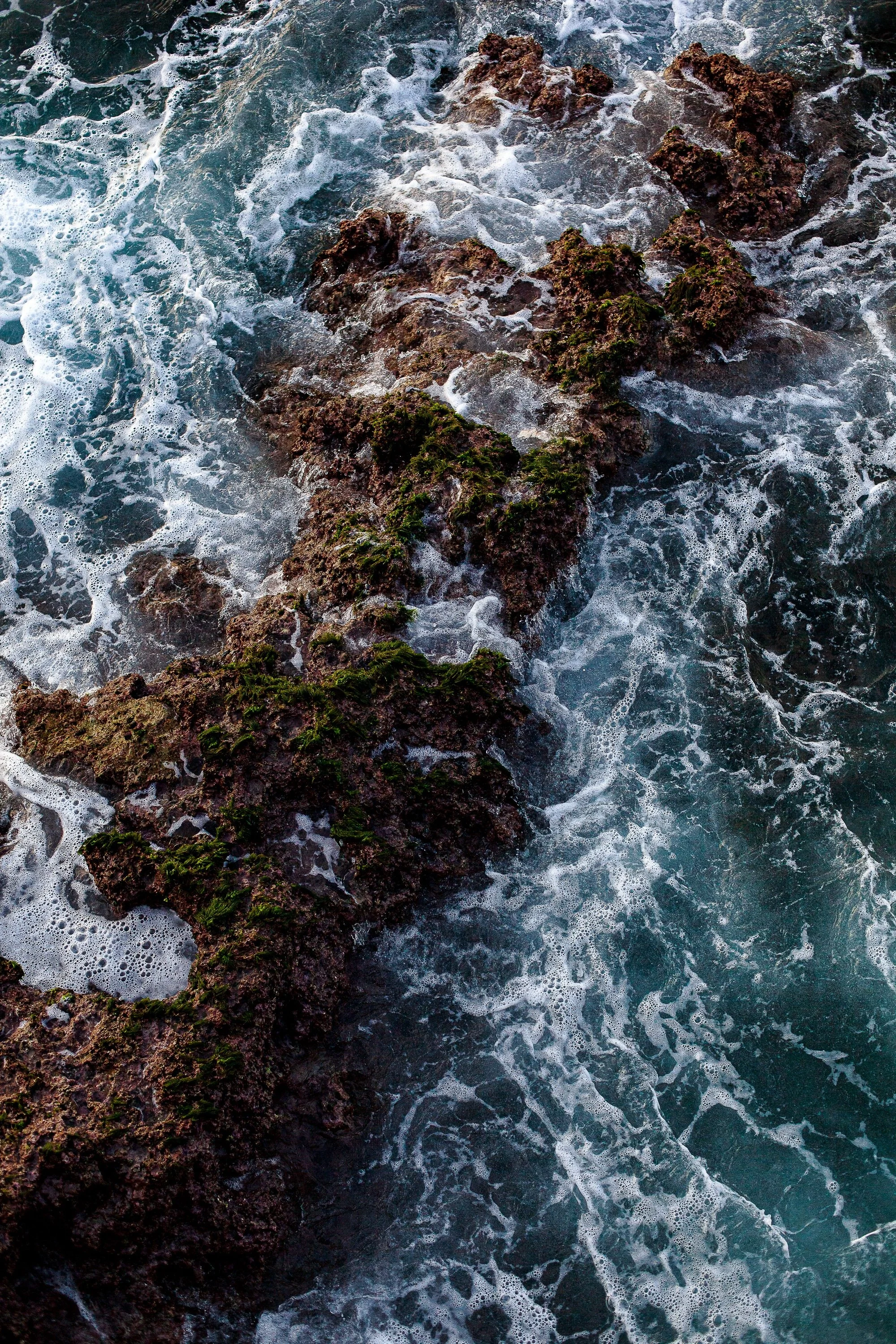 Complete uncropped artwork for Sea Against Stone, showing turquoise water and white foam churn around dark coastal rock in an overhead vertical view