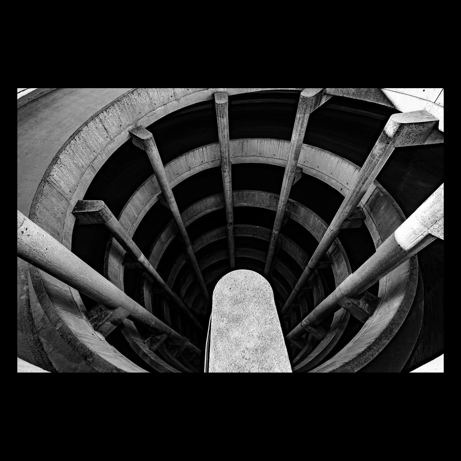 Full-frame black presentation thumbnail of Spiral Descent, showing a black-and-white concrete spiral ramp curves around a bright central pier