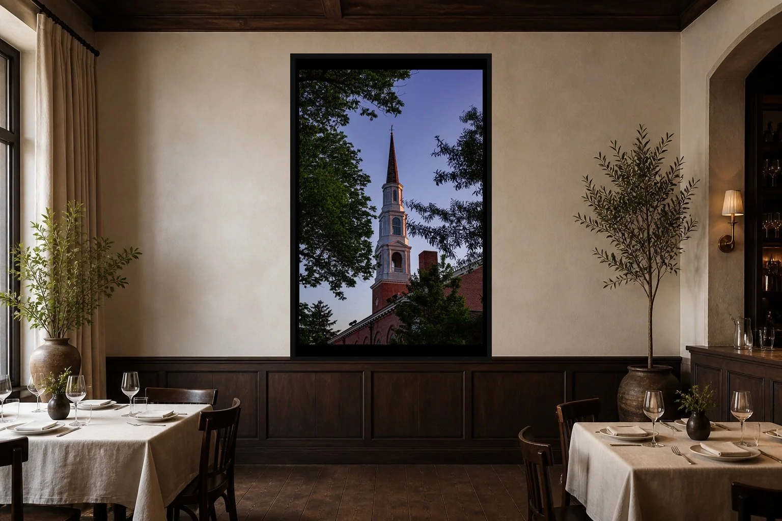 Steeple at Blue Hour displayed in a black frame within an intimate fine-dining room with plaster walls, dark wood, linen tables, no guests, and a clear central wall