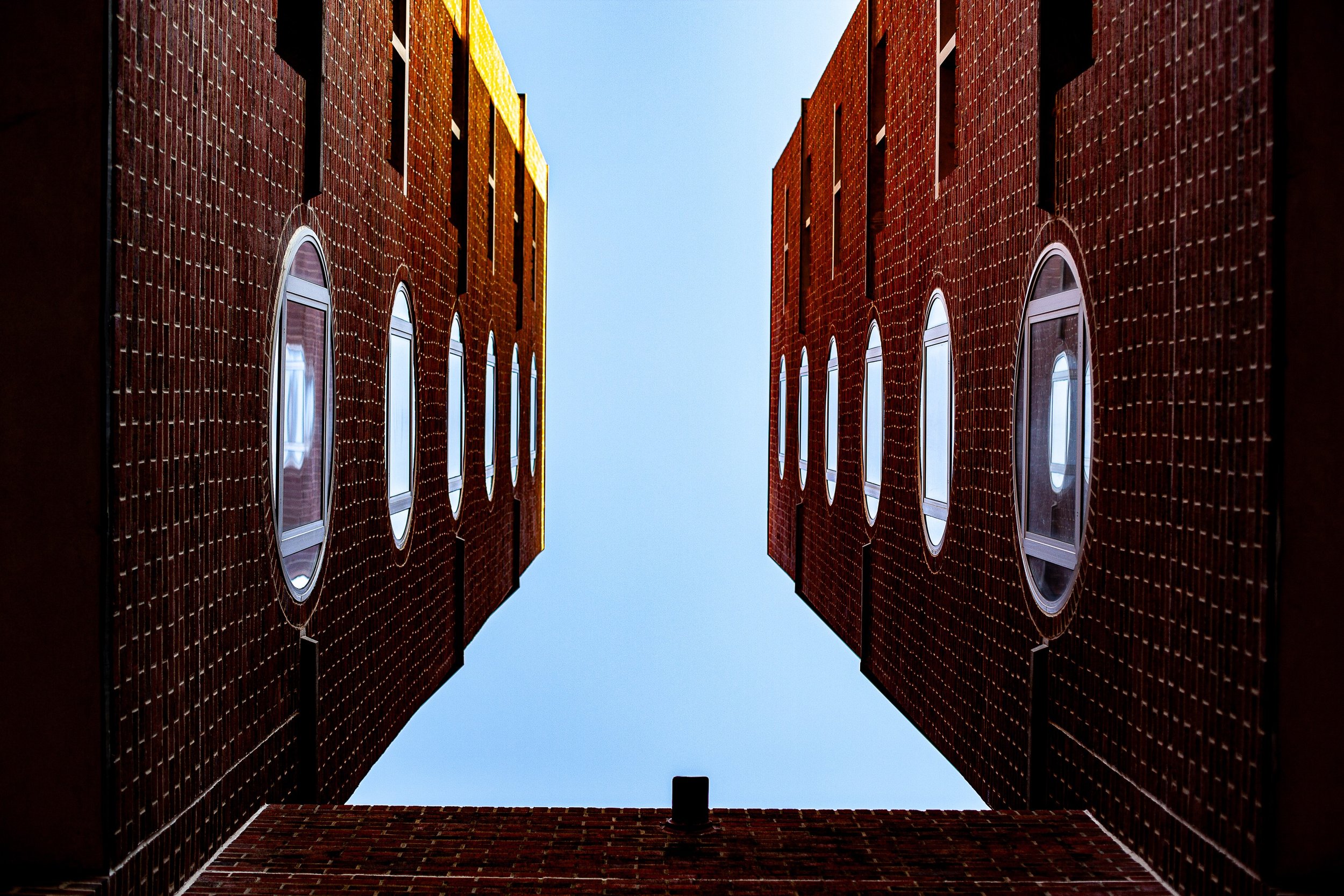 Complete uncropped artwork for Sky Courtyard, showing three red-brick walls and oval windows frame a clean opening of blue sky