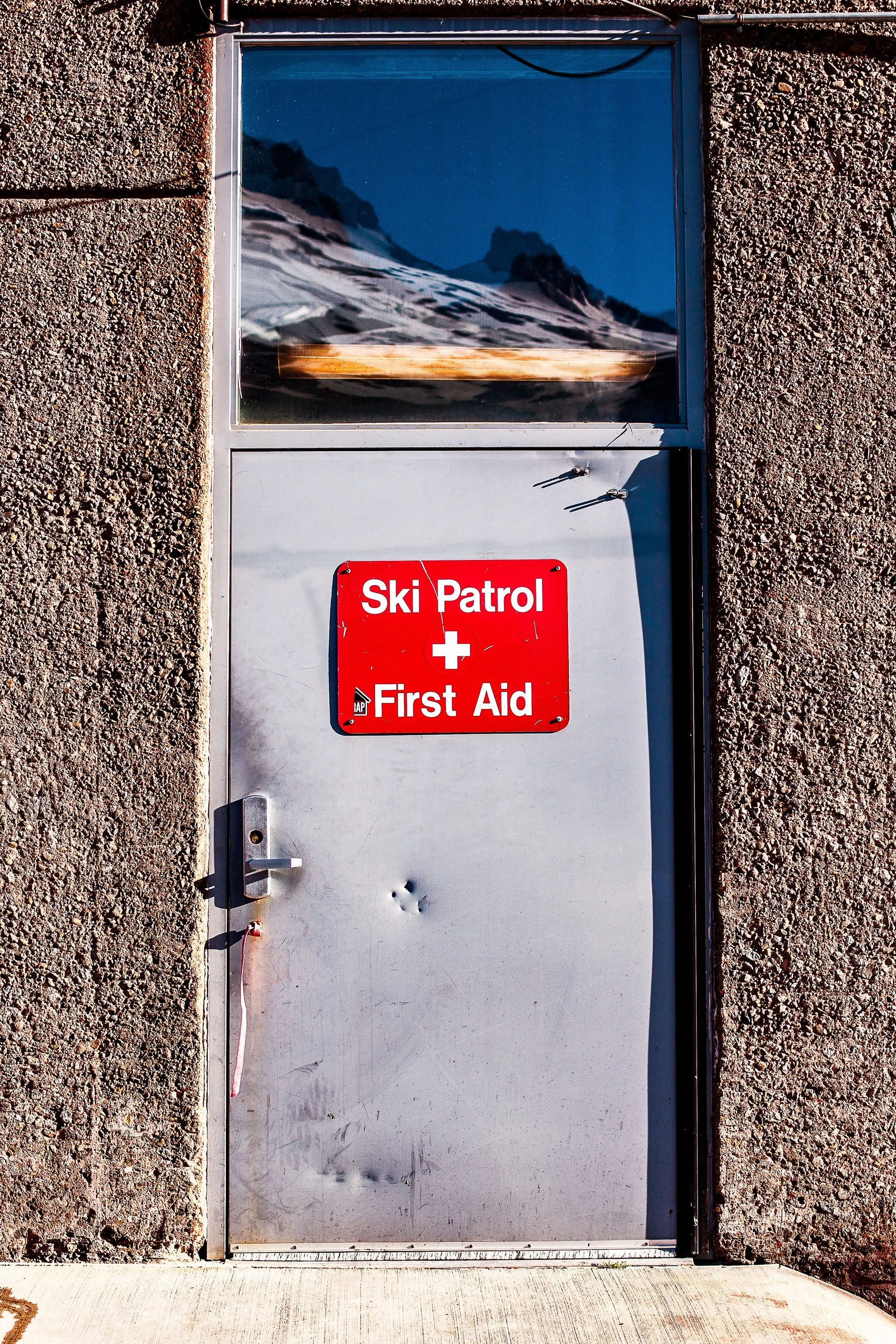 Complete uncropped artwork for First Aid, showing a utilitarian door marked for ski patrol and first aid stands beneath a small mountain image