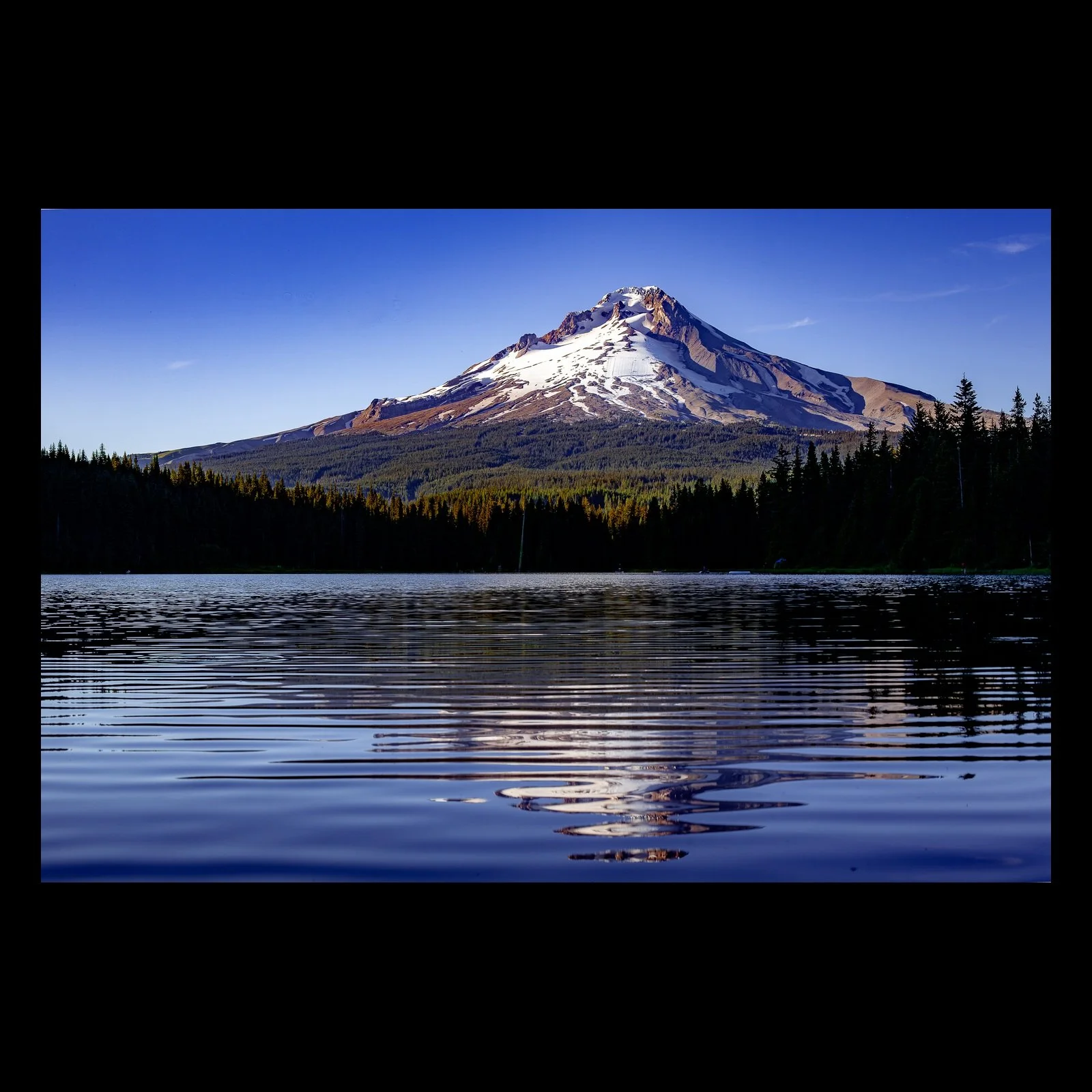 Full-frame black presentation thumbnail of Mountain in Reflection, showing a snow-touched mountain rises above a dark forest and reflects in calm blue water