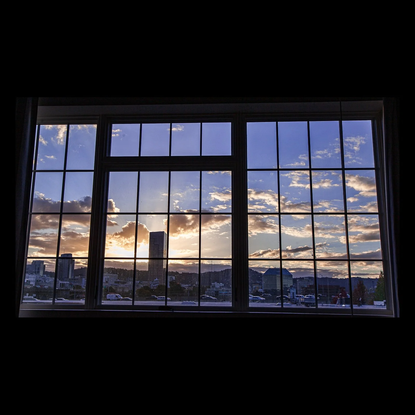 Full-frame black presentation thumbnail of Window Weather, showing a sunset and scattered clouds are divided by the dark grid of a large industrial window