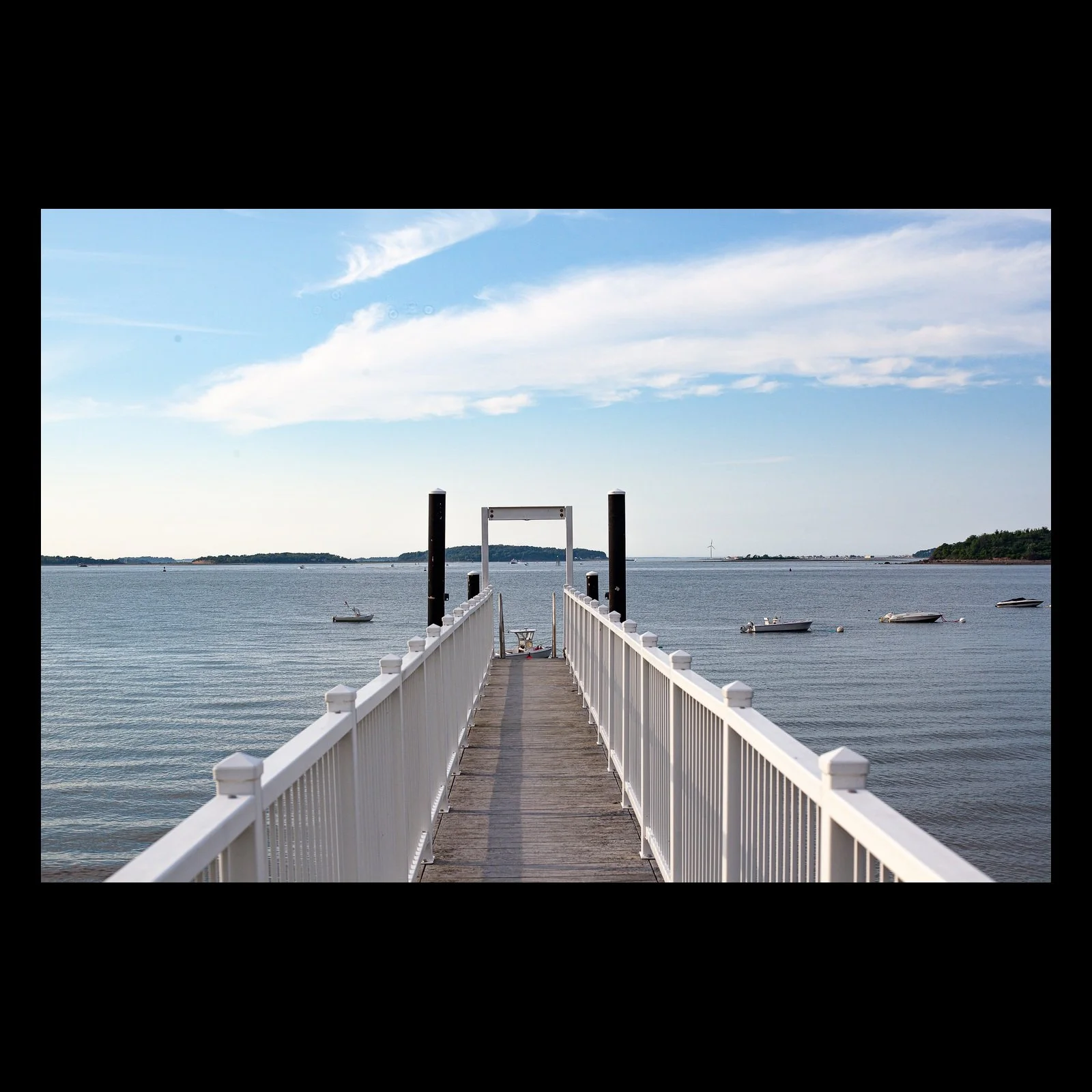 Full-frame black presentation thumbnail of Walk to the Water, showing a long white-railed dock leads directly toward calm open water and small anchored boats