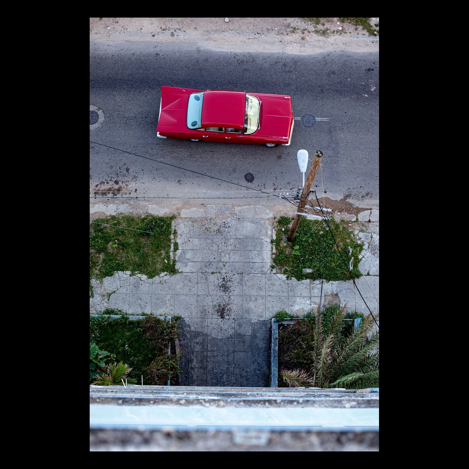 Full-frame black presentation thumbnail of 59 Impala, showing a small red car is viewed straight down beside pale pavement and an empty concrete path