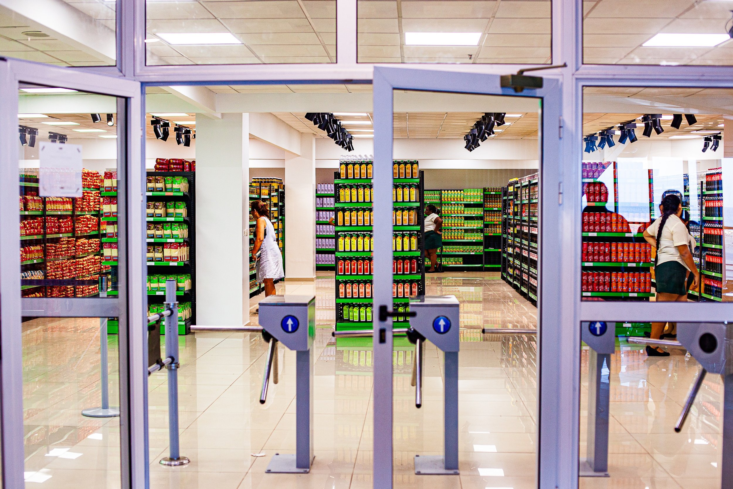 Complete uncropped artwork for The Threshold, showing glass entry gates frame a brightly ordered shop interior filled with colorful rows